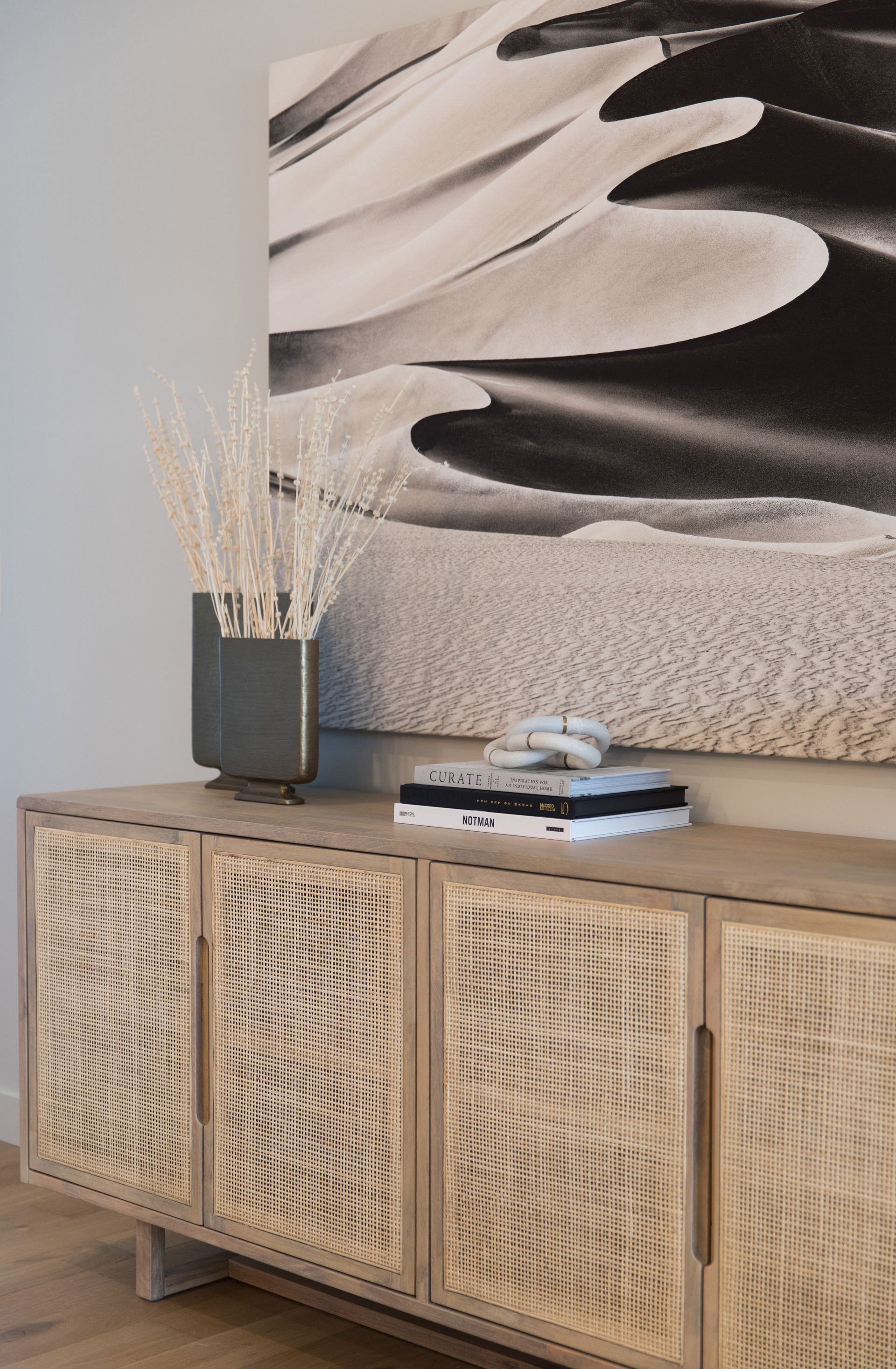 A wooden cabinet with wicker doors and a painting on the wall above it.