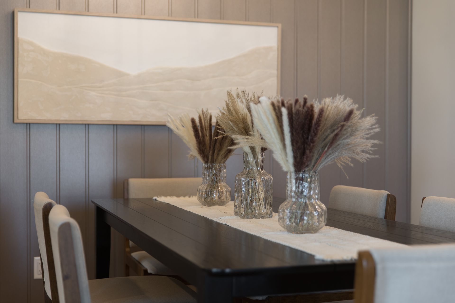 A dining room table with vases of dried flowers on it.
