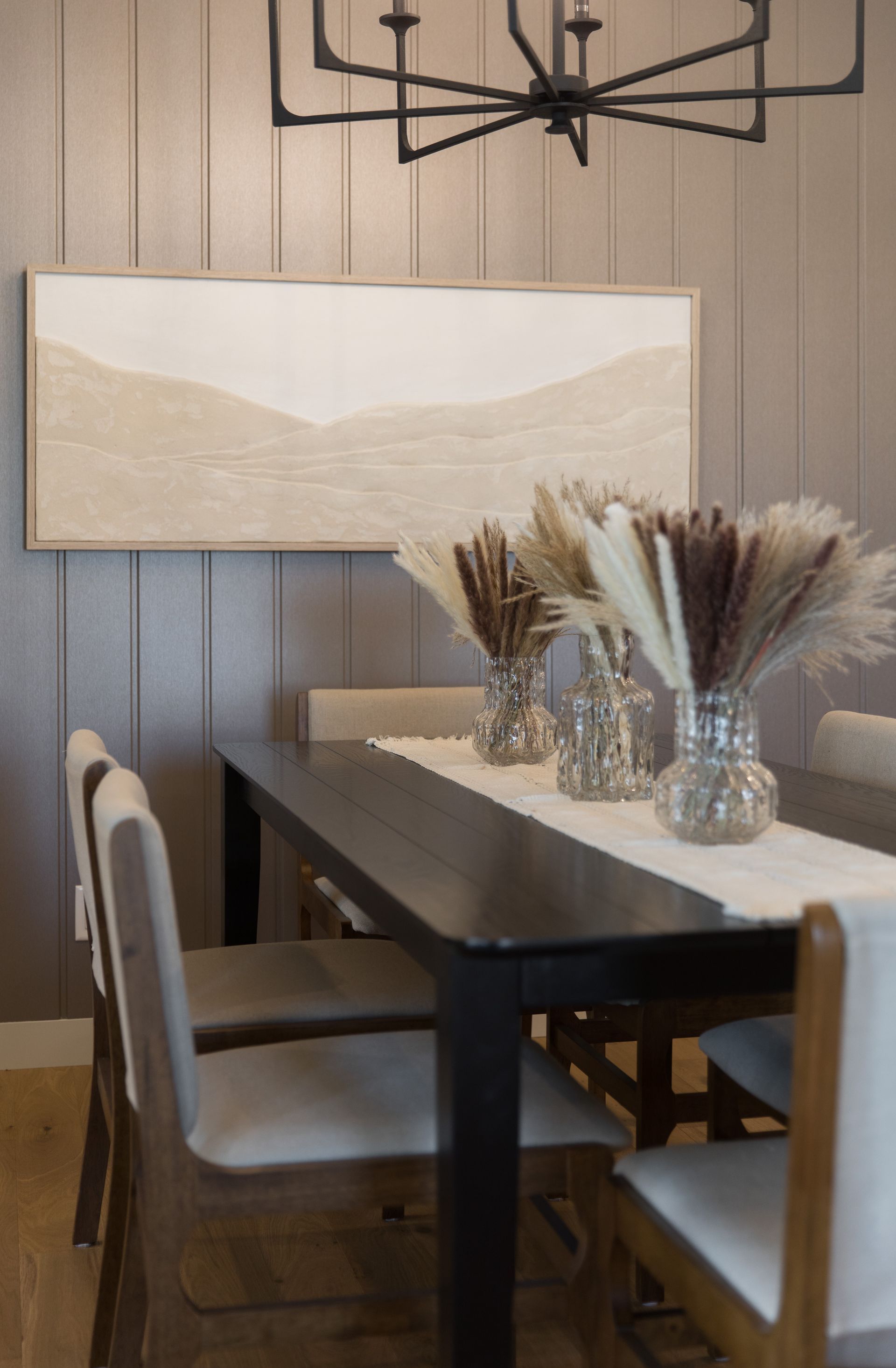 A dining room table with vases of dried flowers on it.