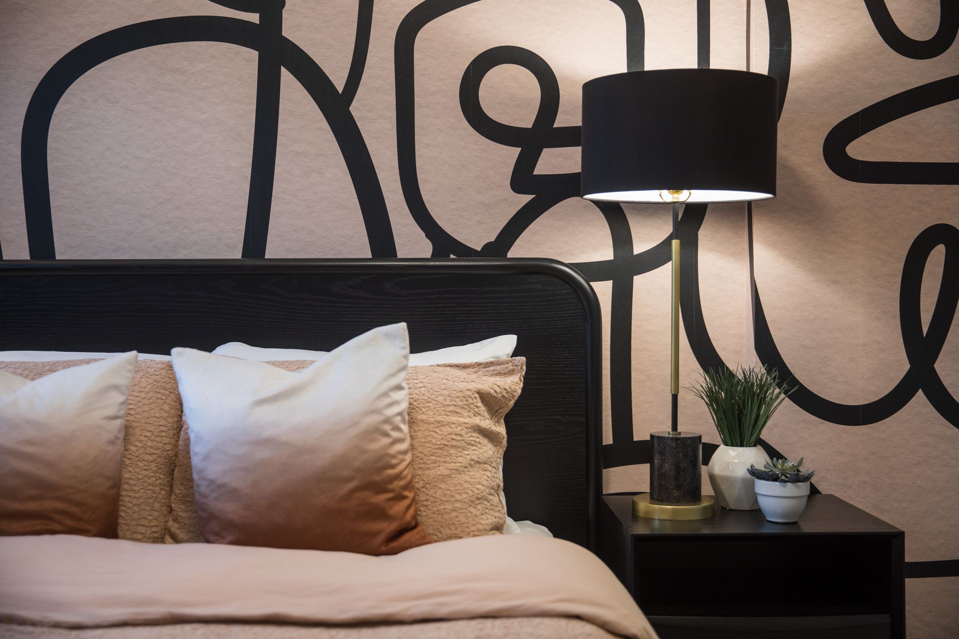 A bedroom with a bed , nightstand , lamp and a painting on the wall.