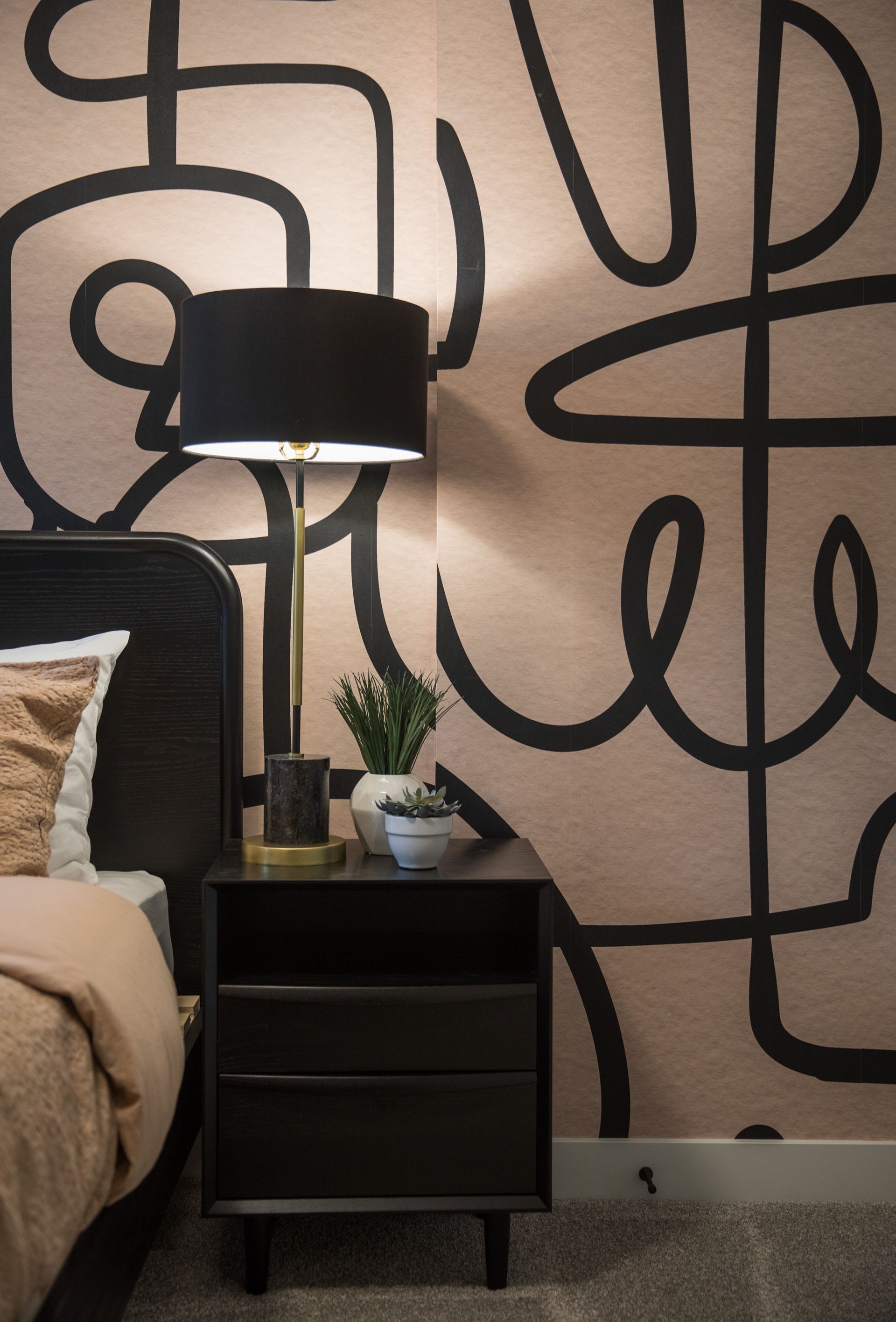 A bedroom with a bed , nightstand , lamp and a painting on the wall.