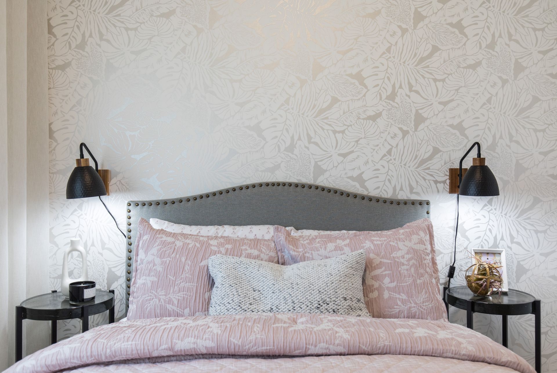 A bedroom with a bed , two nightstands , and a wall with a patterned wallpaper.