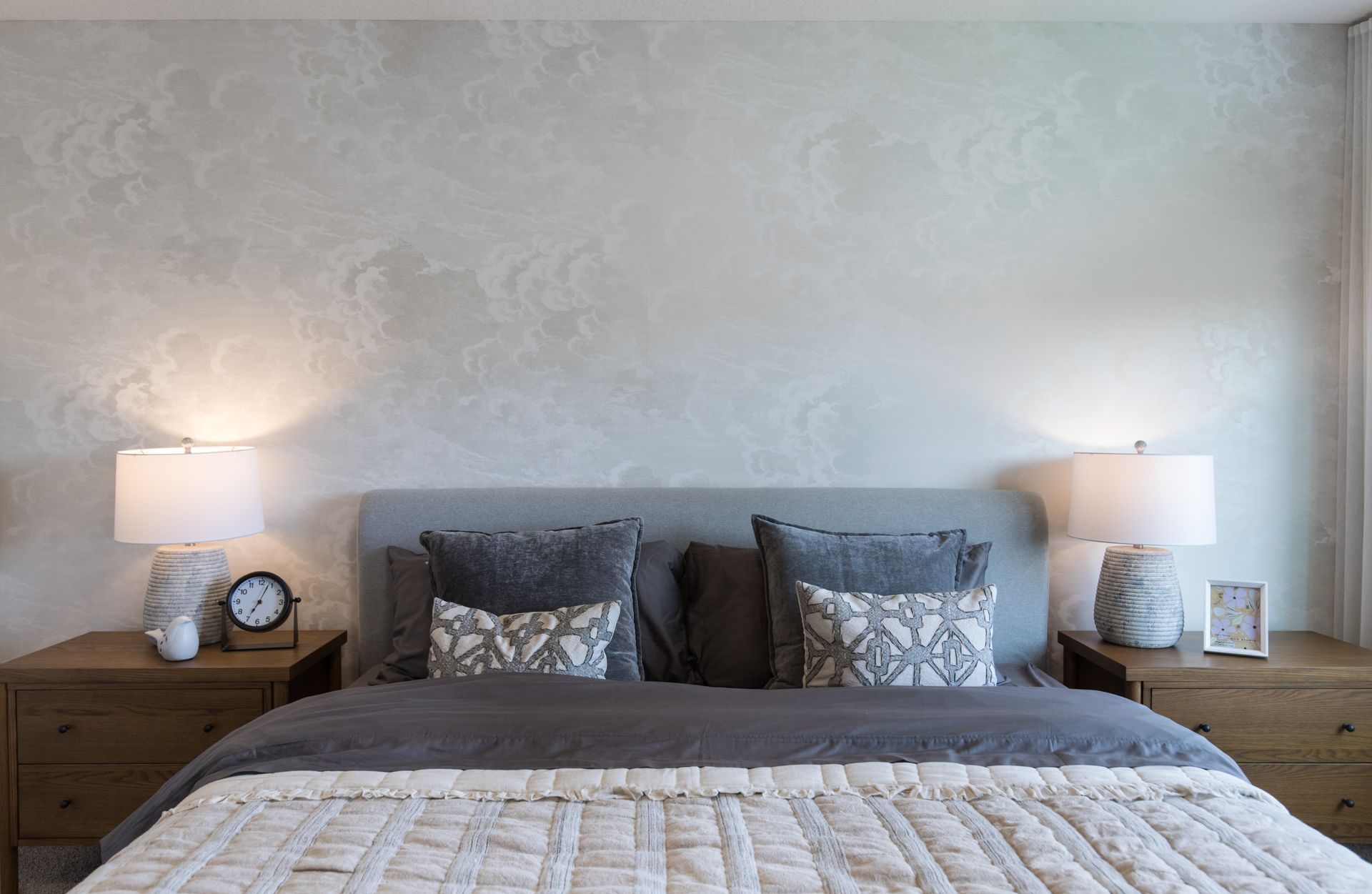 A bedroom with a bed , nightstands , lamps and a clock on the wall.