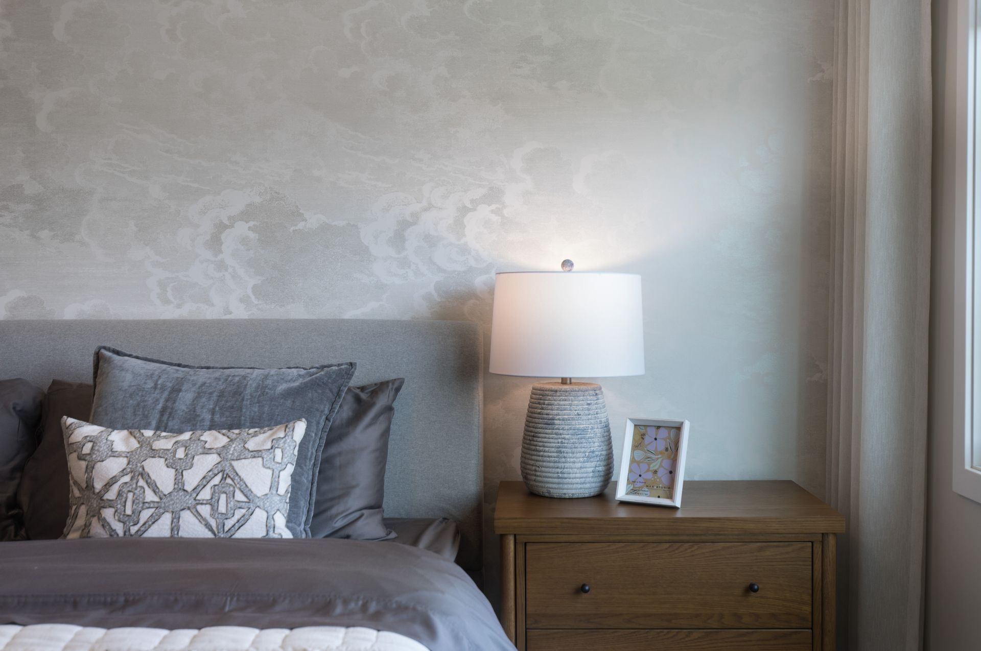 A bedroom with a bed , nightstand , lamp and picture frame.