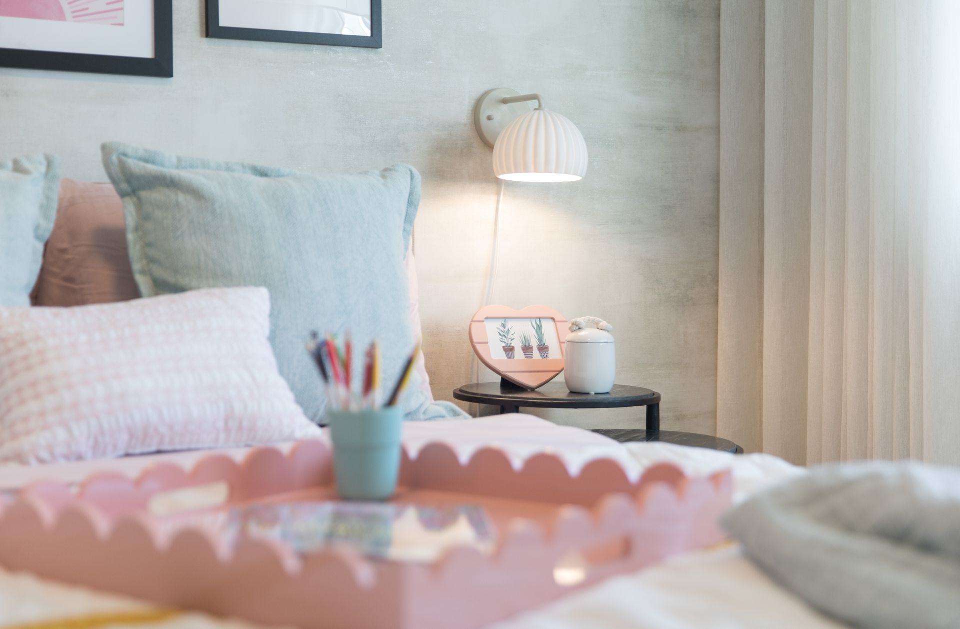 There is a pink tray on the bed with a cup of pencils on it.