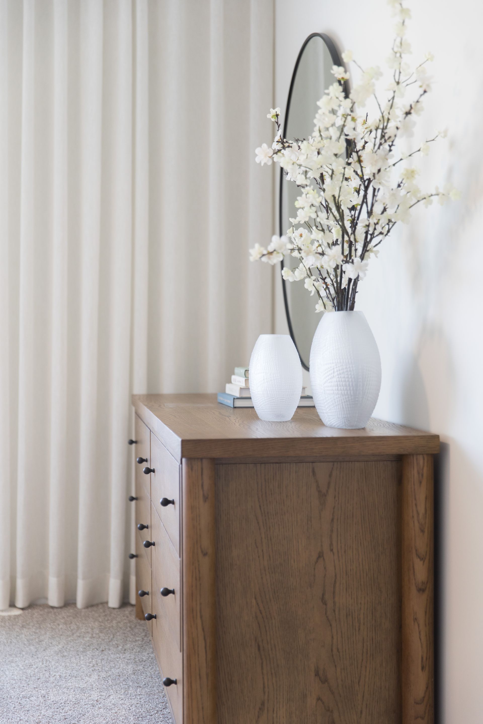 A wooden dresser with two vases of flowers on top of it.