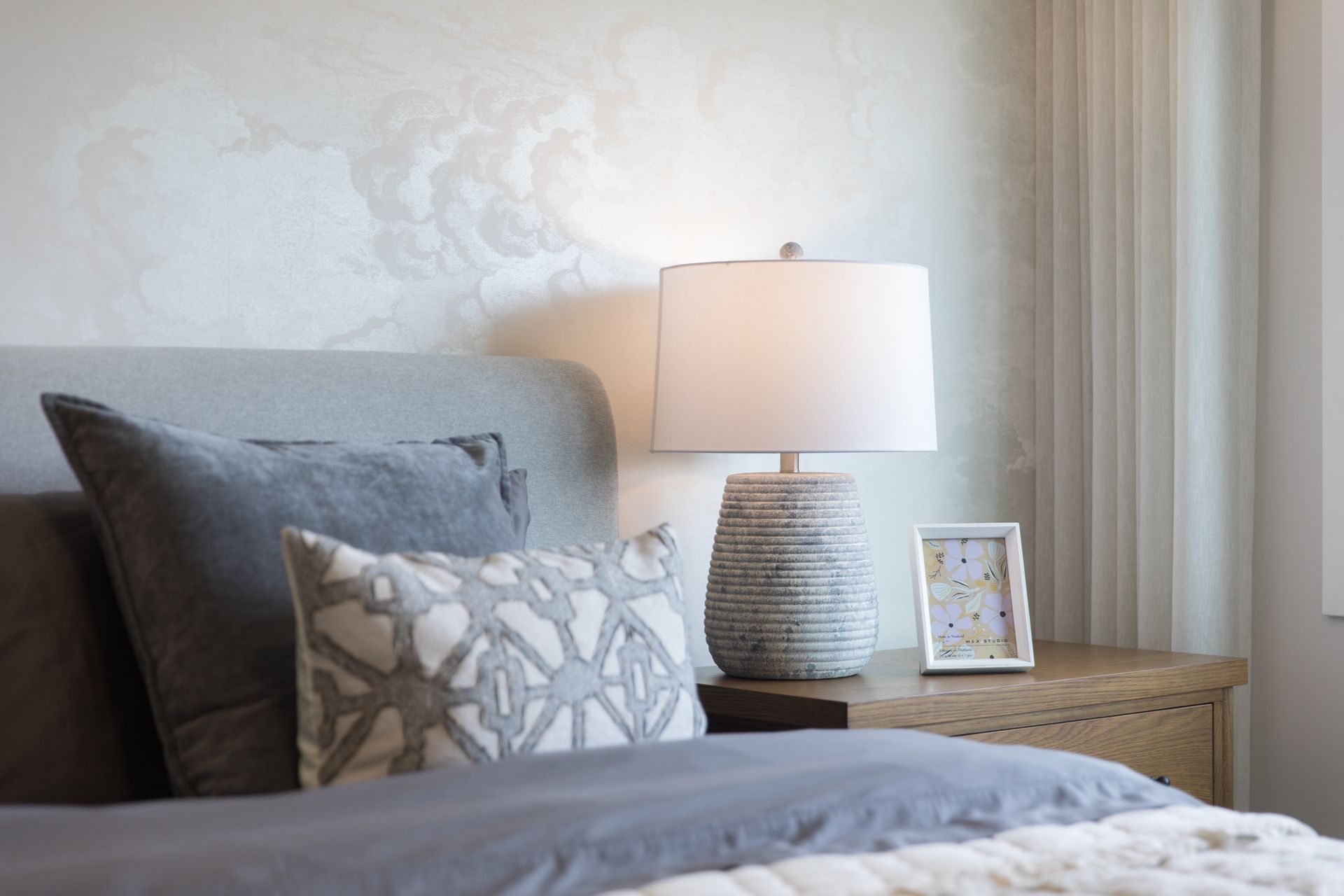 A bedroom with a bed , nightstand , lamp and picture frame.