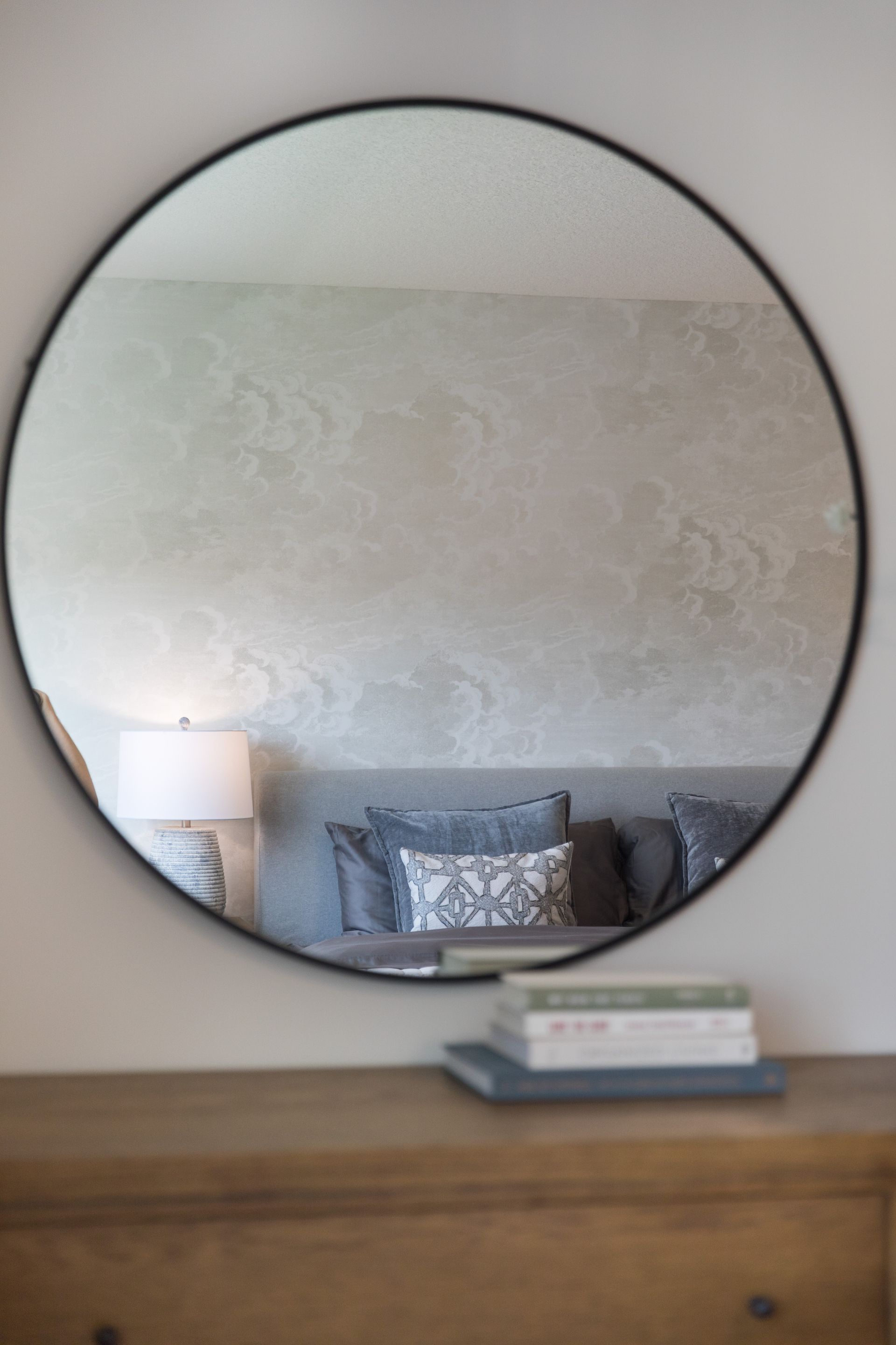 A round mirror is hanging on a wall above a dresser.