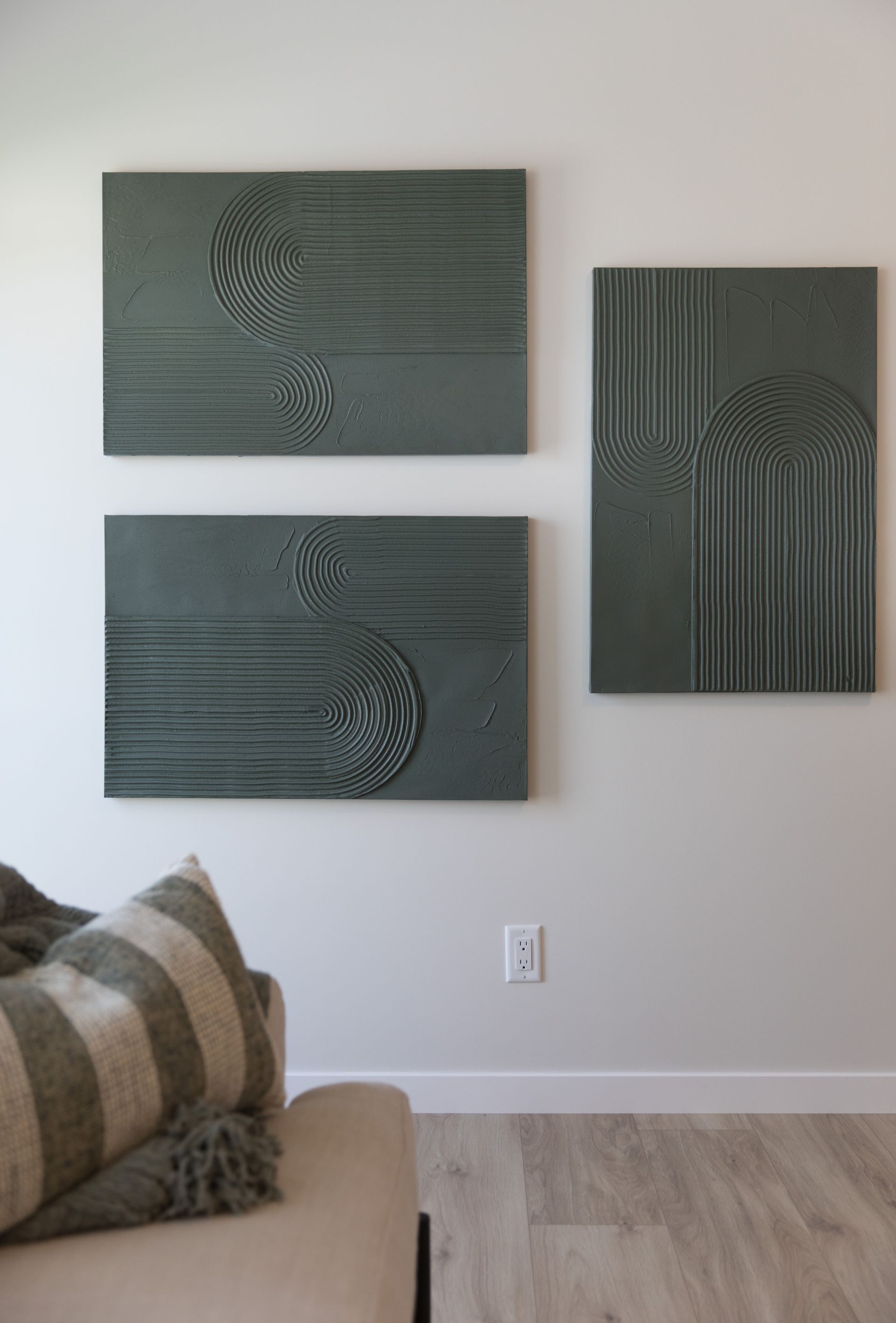 A living room with three paintings on the wall and a couch.