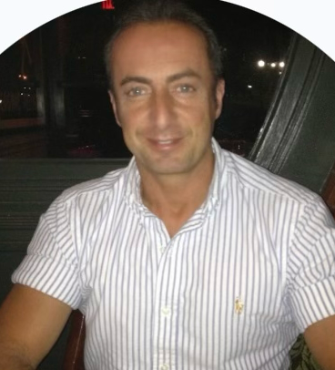 A man with a beard is wearing a white shirt and smiling.