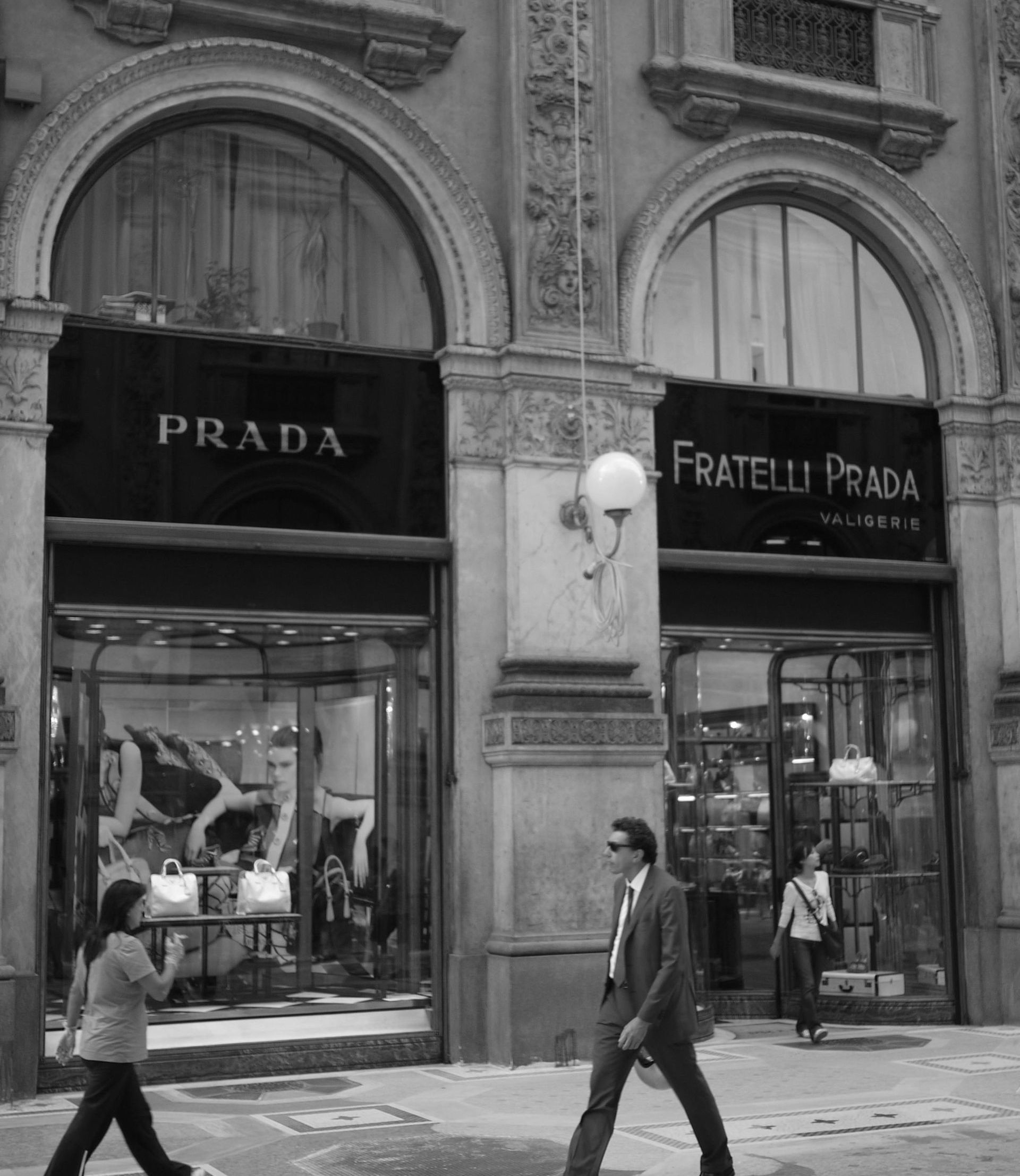 A black and white photo of people walking in front of a prada store