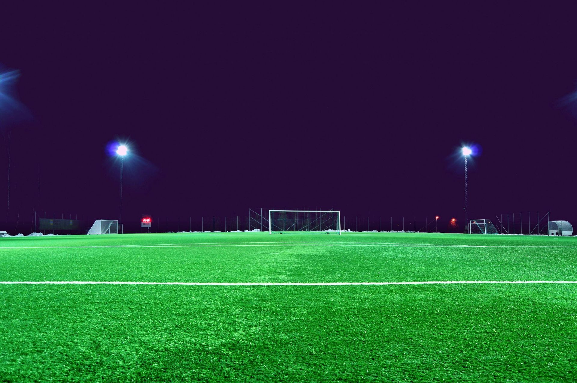 A soccer field is lit up at night with a goal in the background.