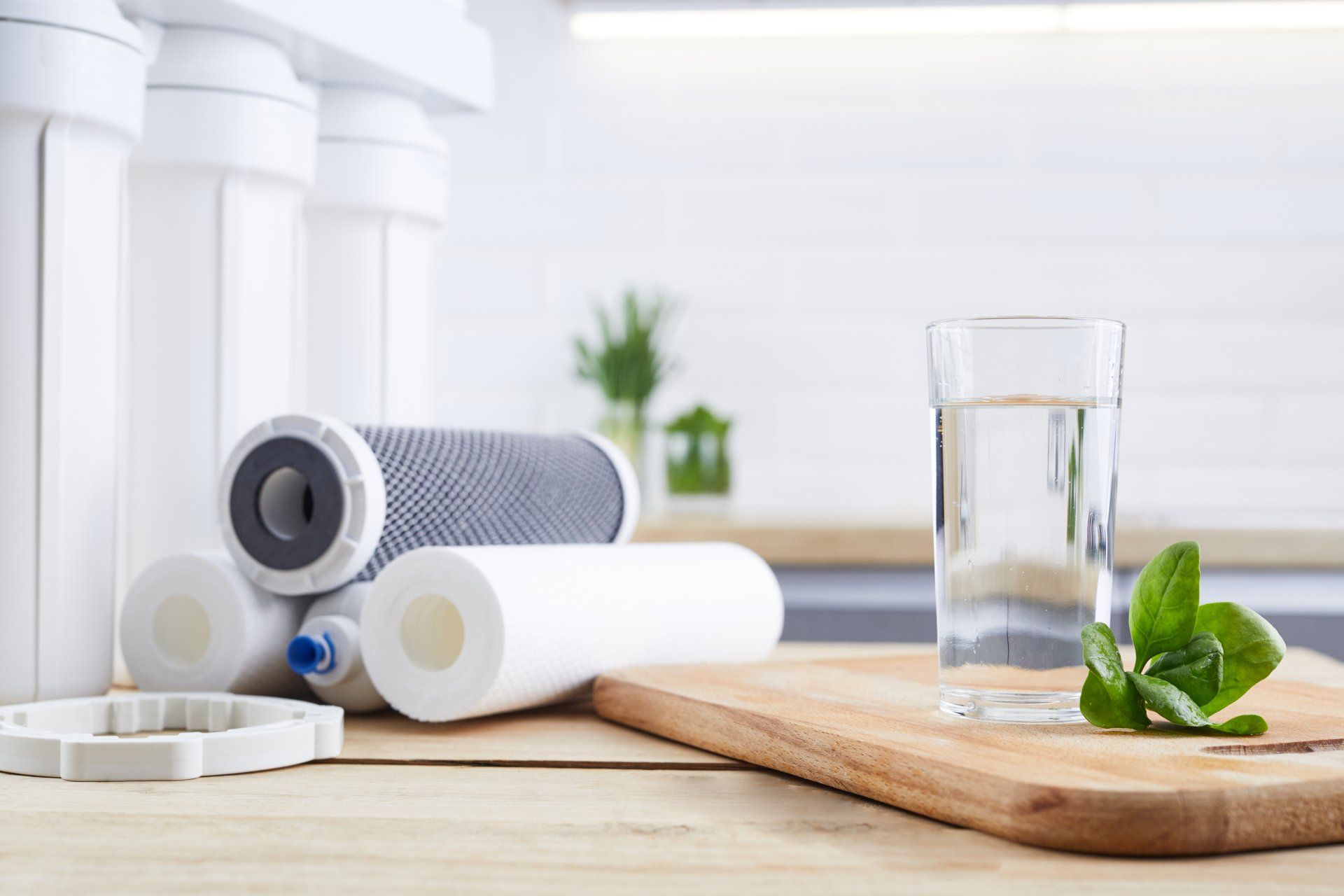A glass of clean water with osmosis filter, green leaves and cartridges on wooden table in a kitchen interior. Concept Household filtration system.