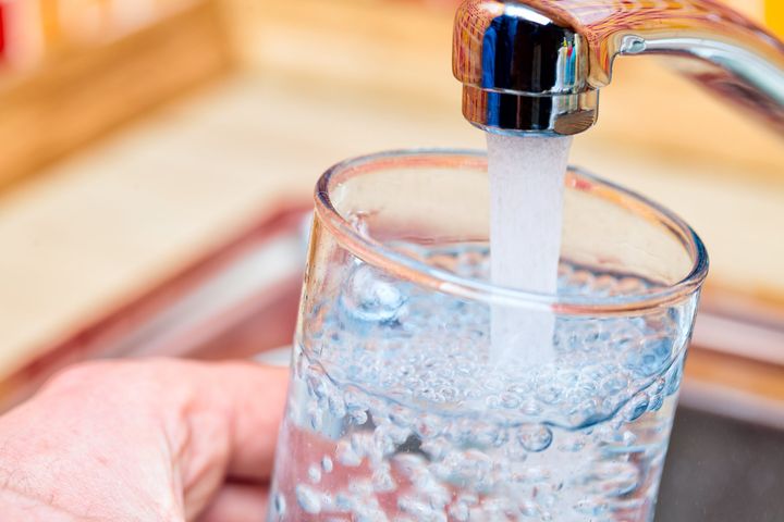 Closeup shot of a man pouring a glass of fresh water from a kitchen faucet