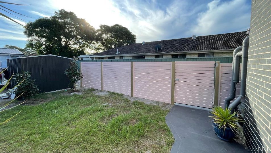 A Pink Fence Next to a Green Lawn — Pride Carpentry & Maintenance In Berkeley Vale, NSW