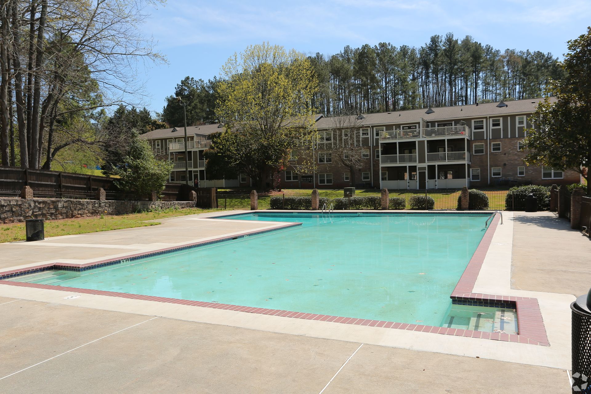 Outdoor swimming pool beside a two-story apartment building with trees and lounge chairs in the background