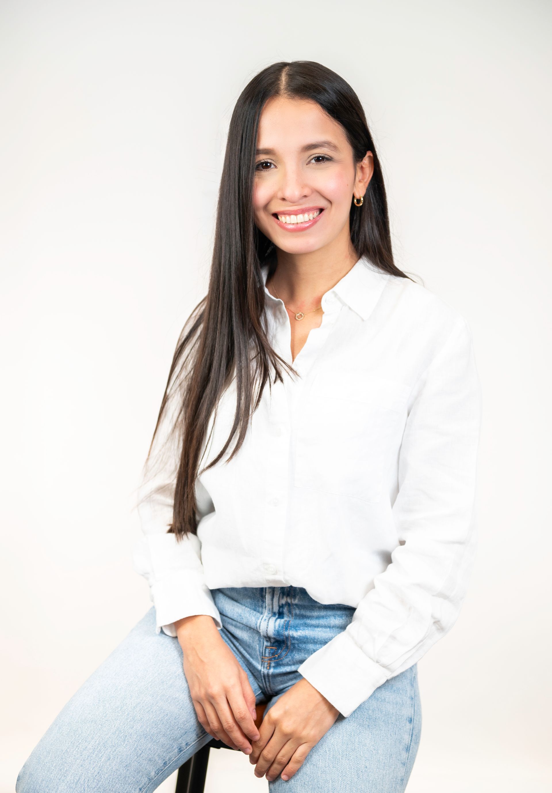 A woman is sitting on a stool wearing a white shirt and jeans.