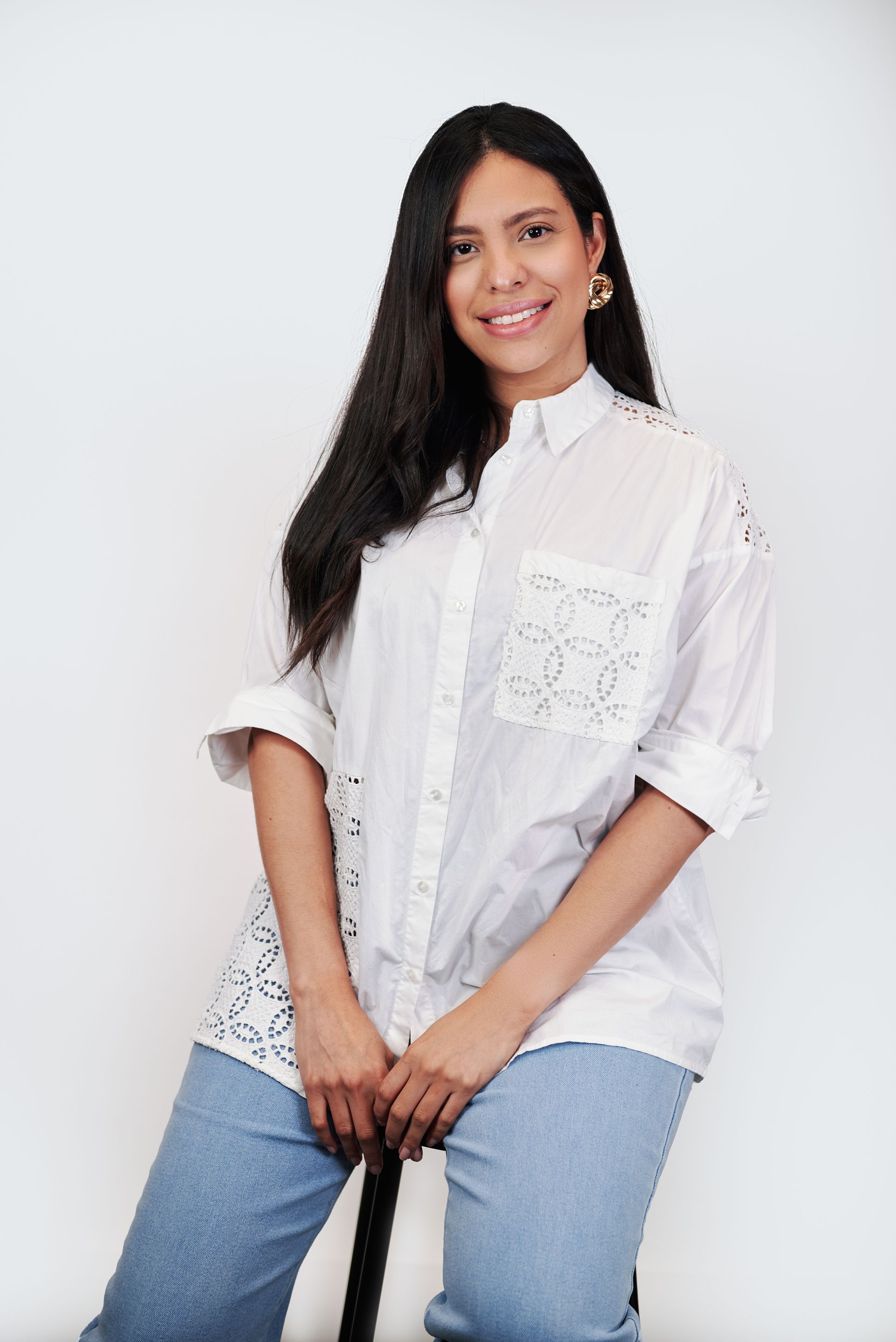 A woman is sitting on a stool wearing a white shirt and blue jeans.