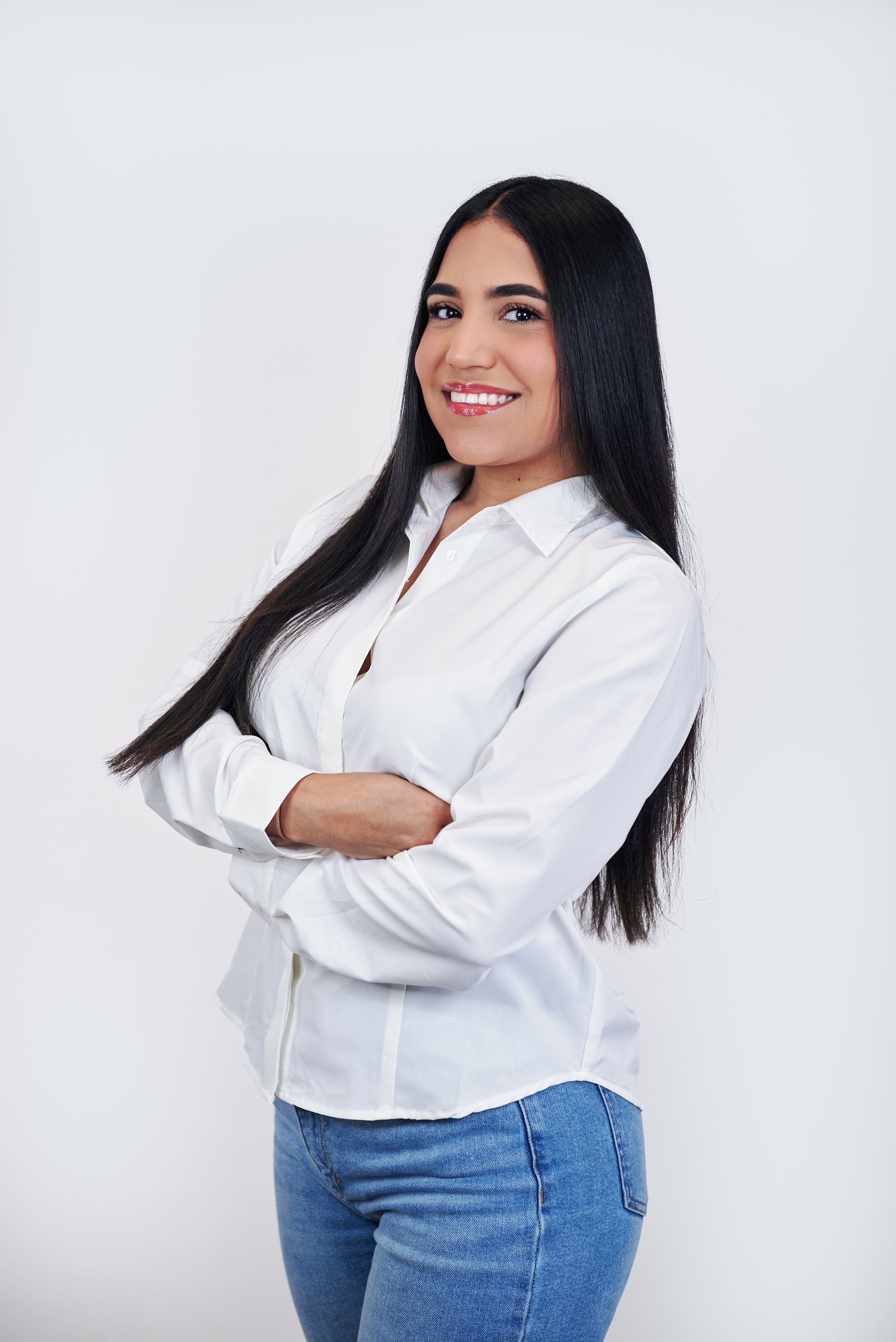 A woman in a white shirt and blue jeans is standing with her arms crossed.