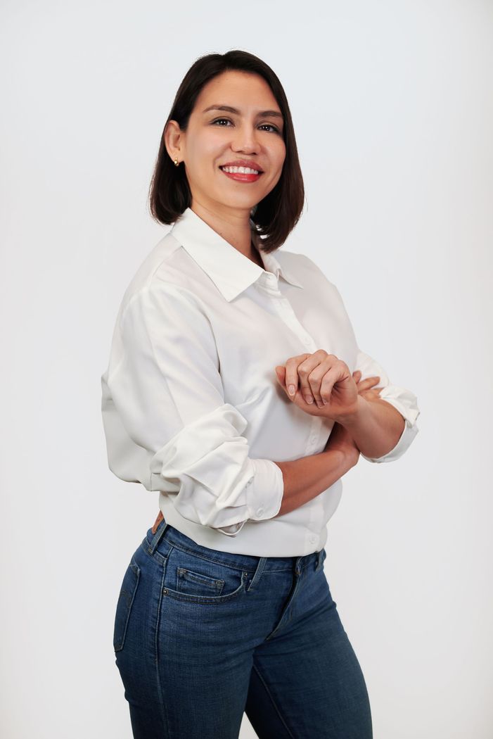 A woman in a white shirt and blue jeans is standing with her arms crossed.