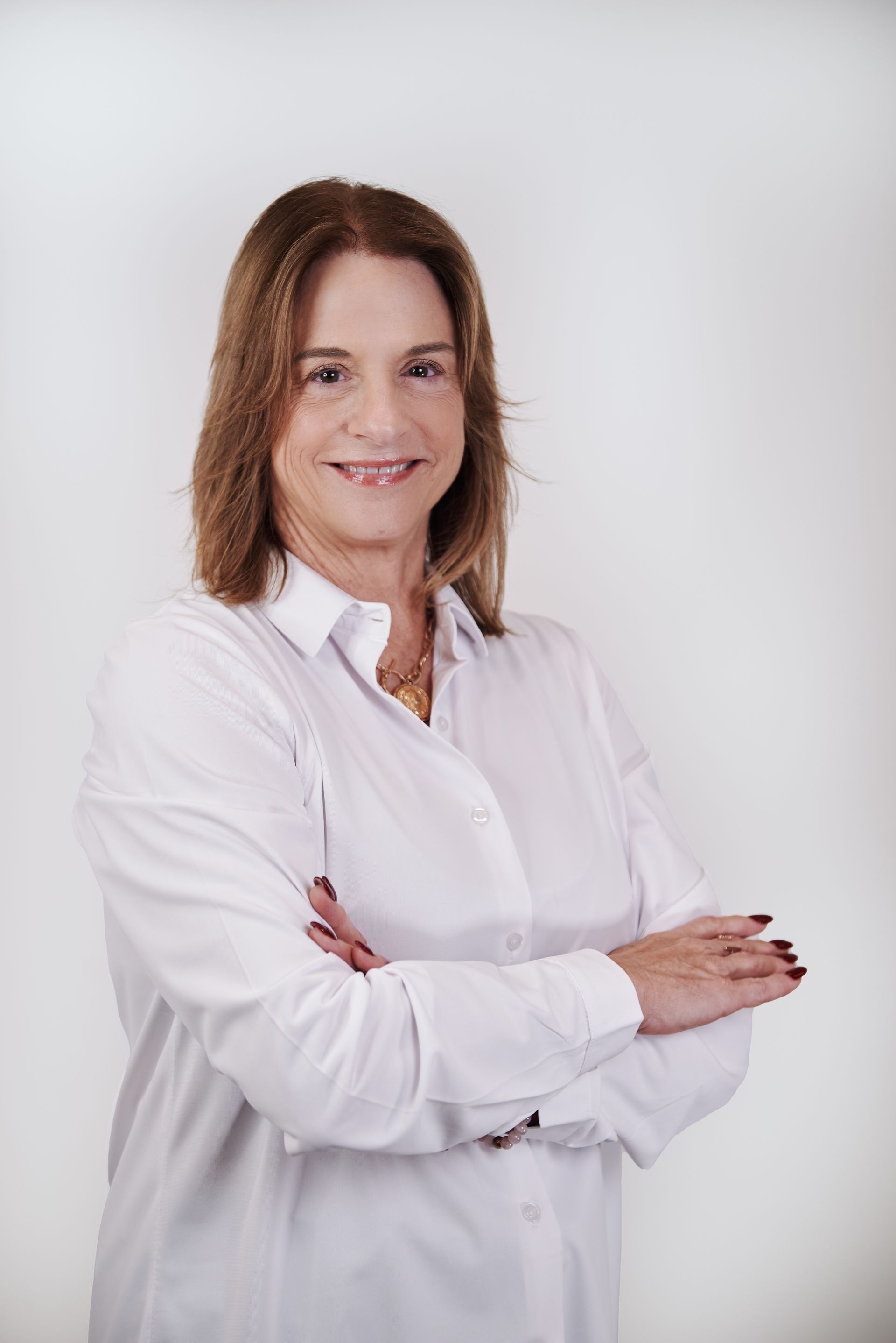 A woman in a white shirt is standing with her arms crossed and smiling.