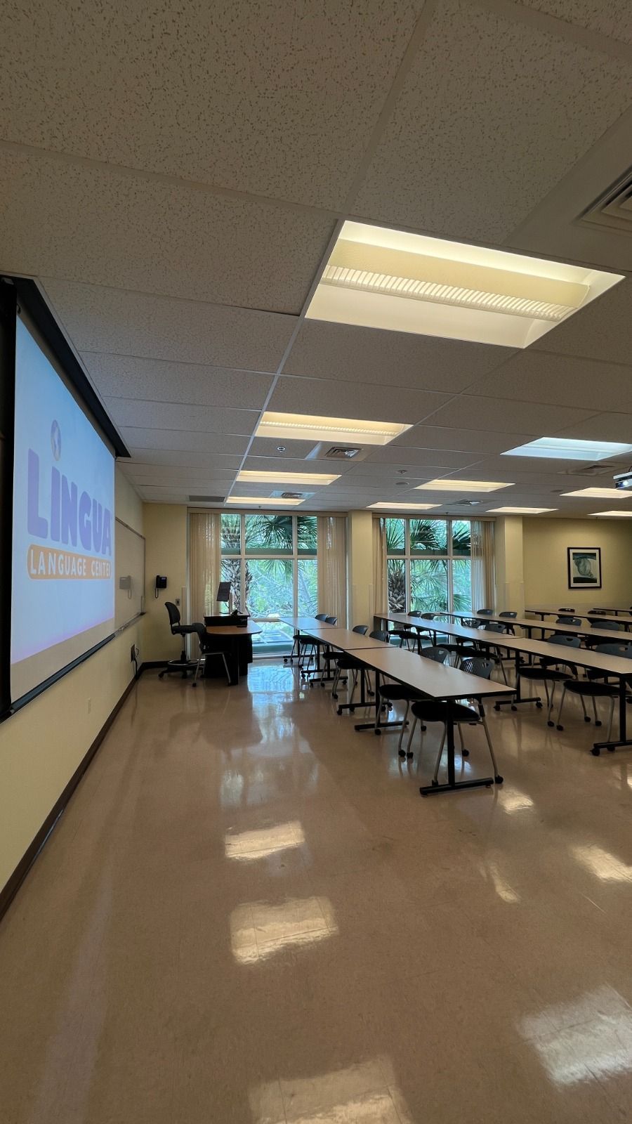 A large classroom with tables and chairs and a projector screen.