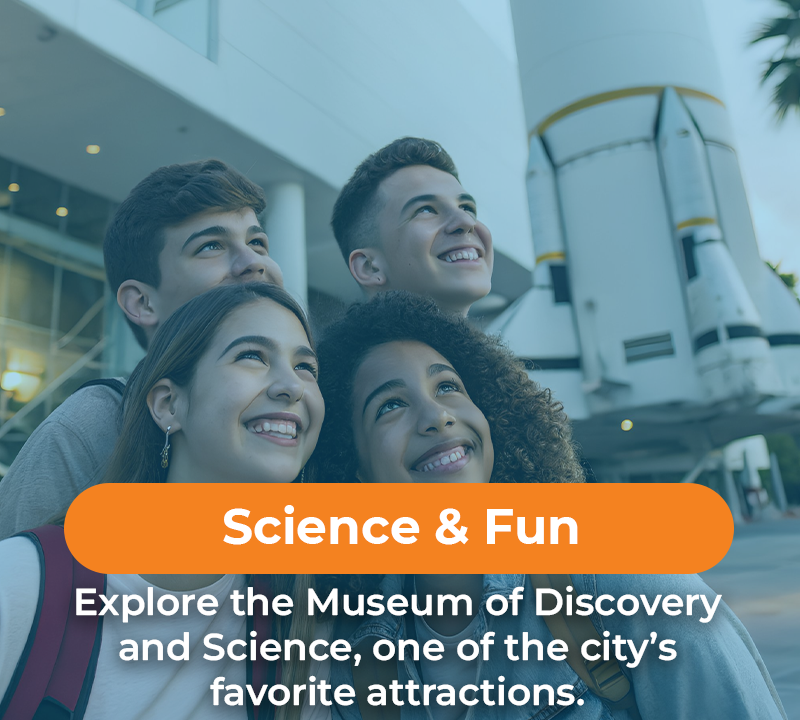 Four smiling teens looking upward in front of a museum and rocket; text overlay