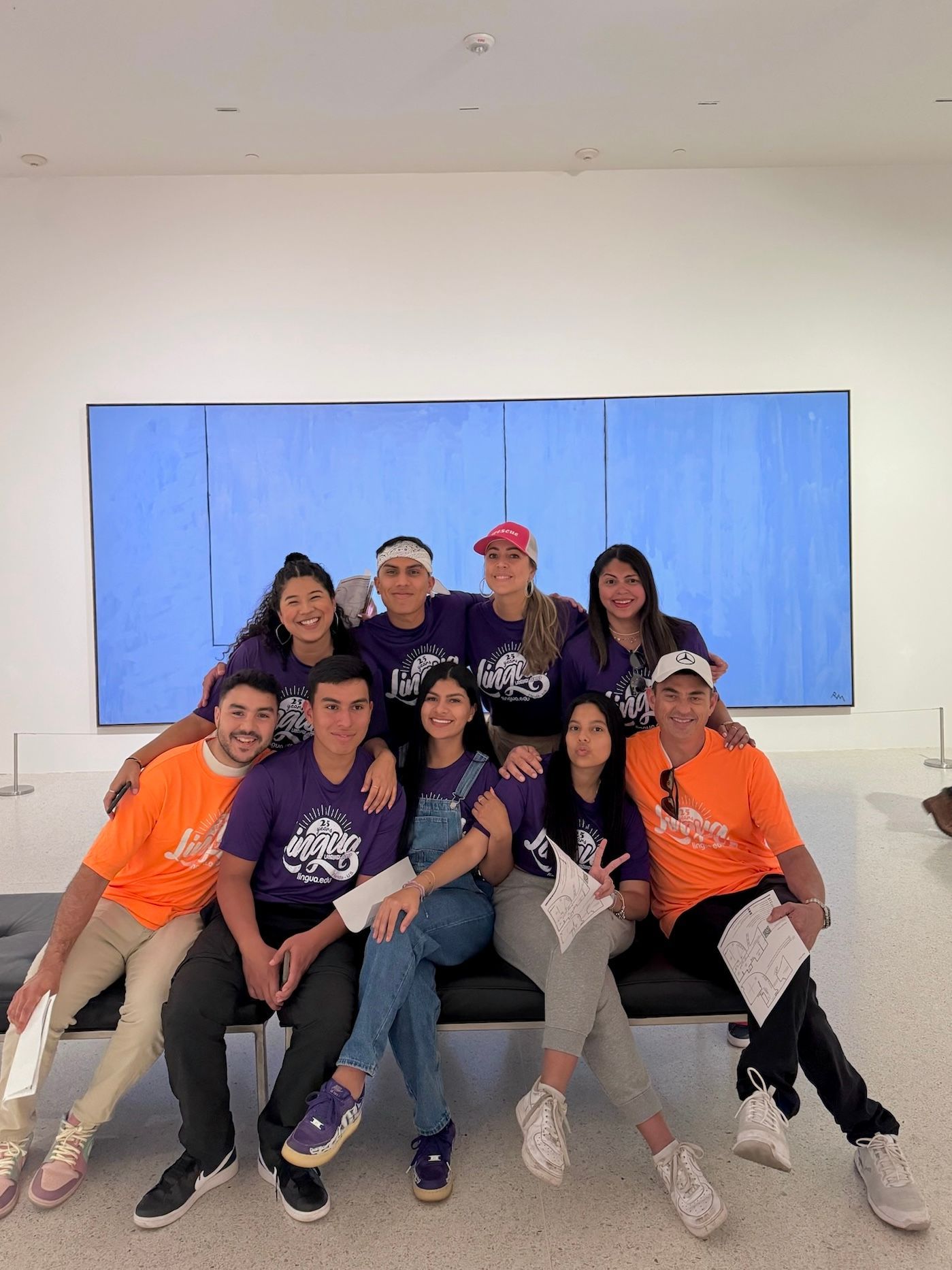 Group of nine people posing and smiling in front of a large blue wall indoors.