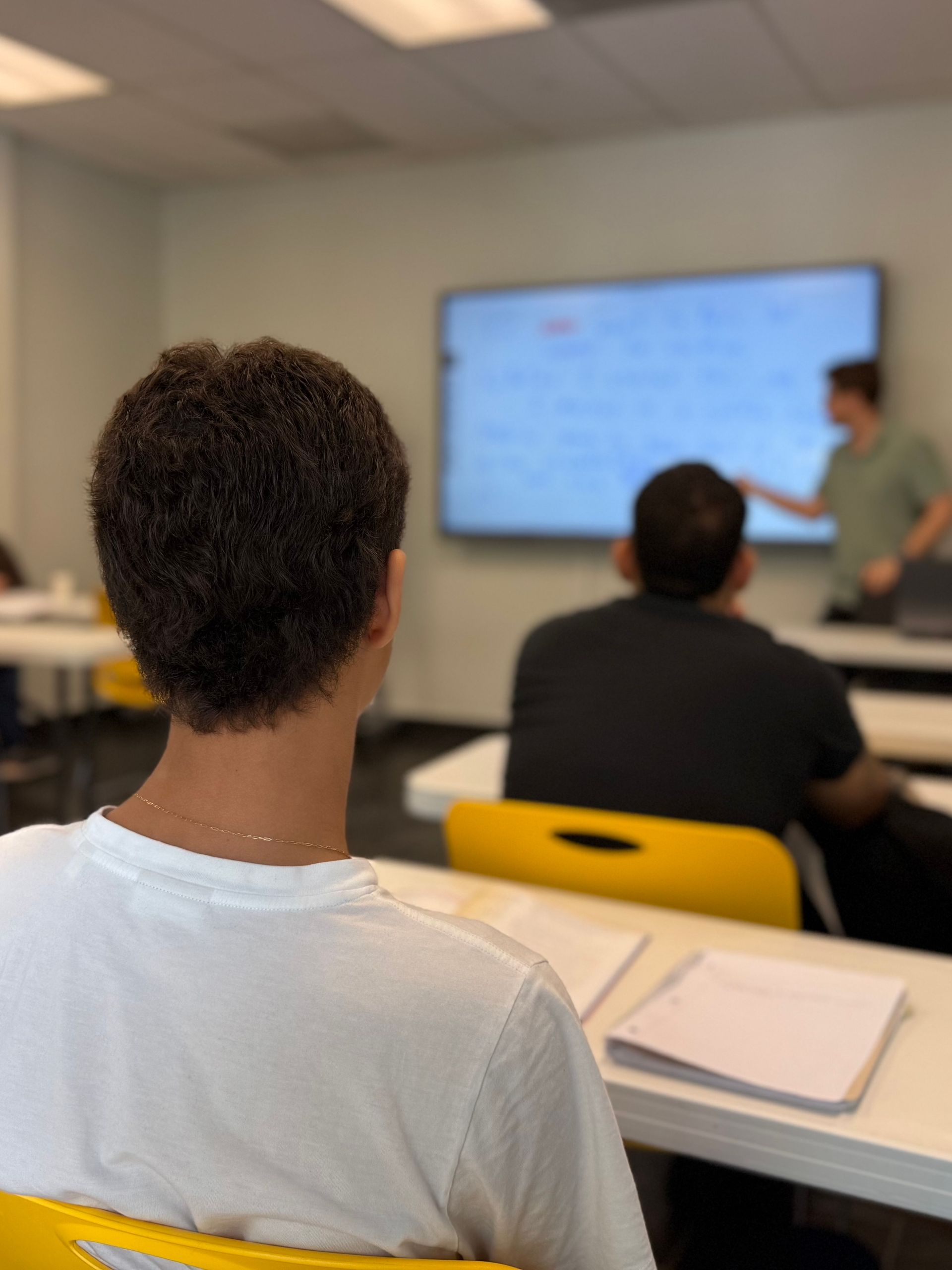 Classroom lecture with students seated and a presenter at a screen in front