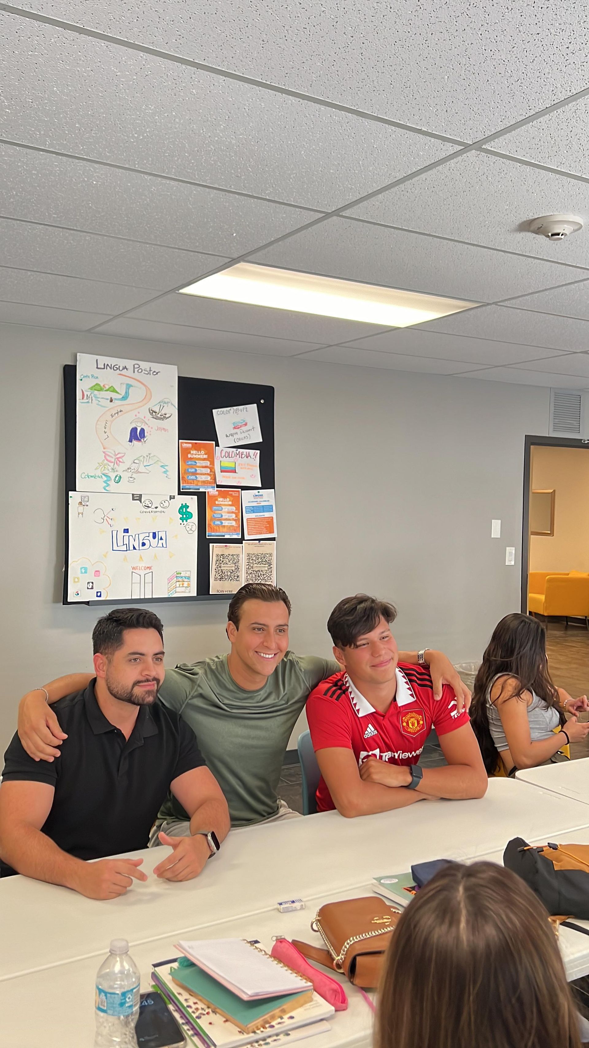 People seated around a conference table in a classroom or meeting room, with bulletin boards and papers on the walls.