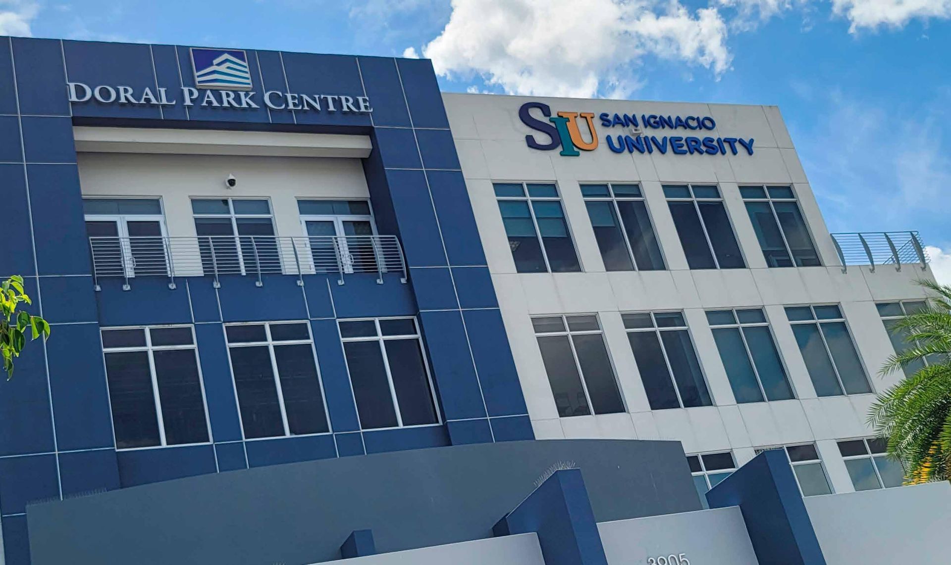 Blue and white university building with glass windows and a partly visible sign under a blue sky