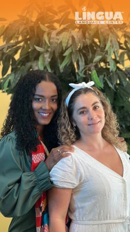 Two women are posing for a picture together in front of a tree.