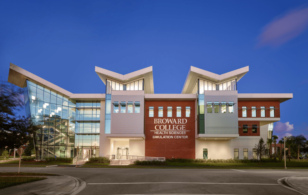 Modern college building exterior at dusk with glass entrance and red brick facade under a blue sky