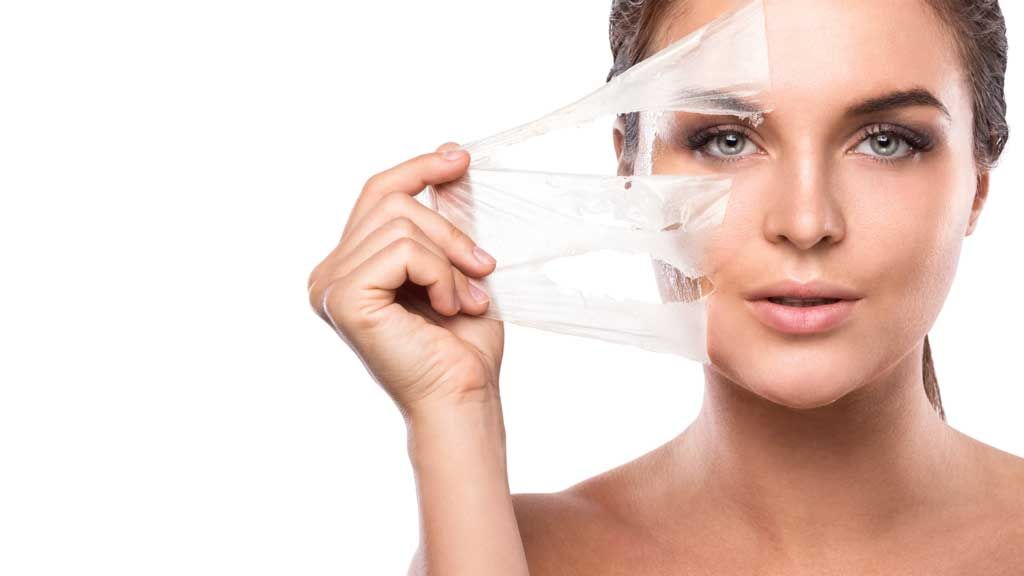 A woman is peeling off a piece of plastic from her face.