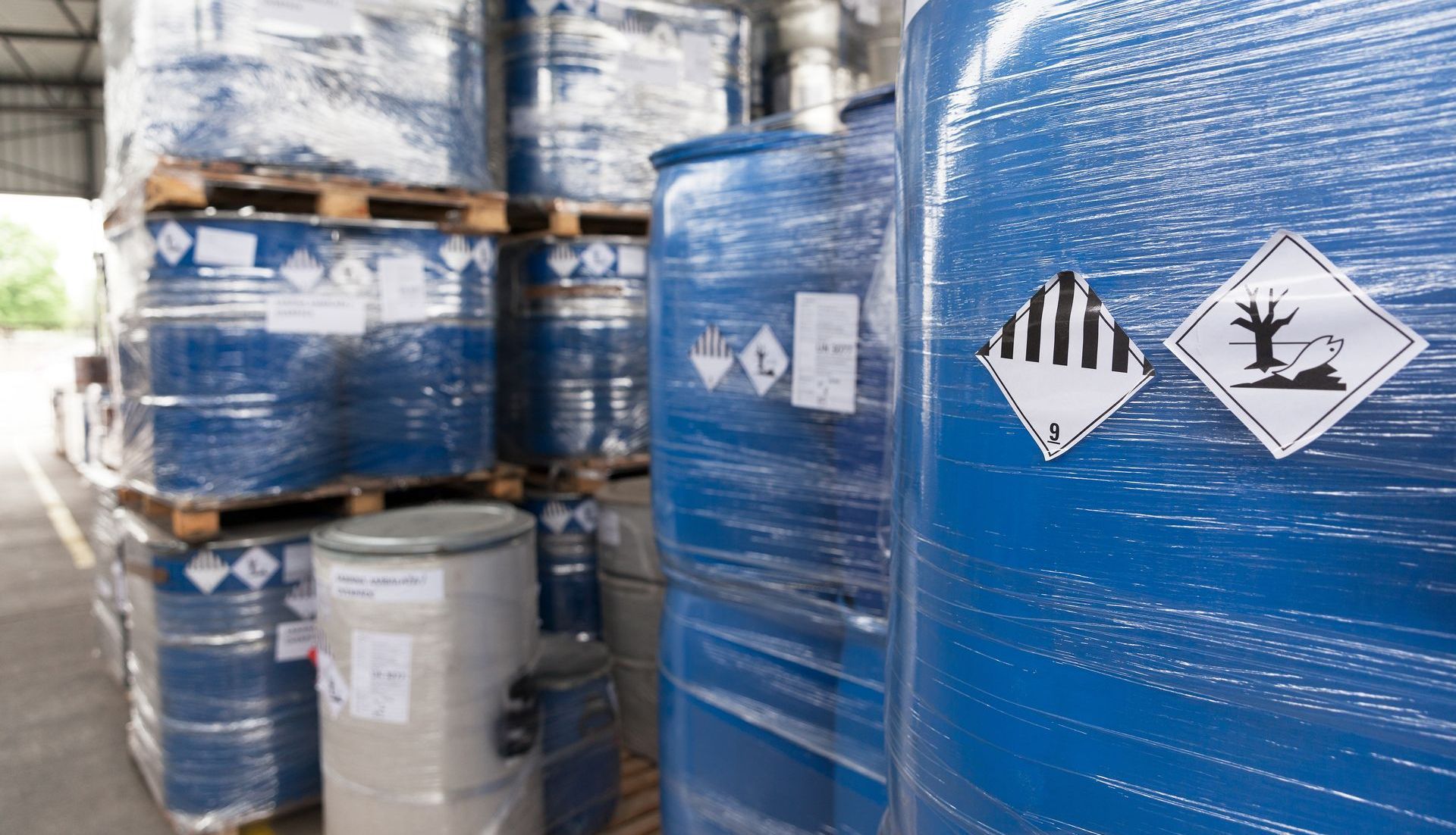 Fûts chimiques bleus avec symboles de danger empilés dans un entrepôt.