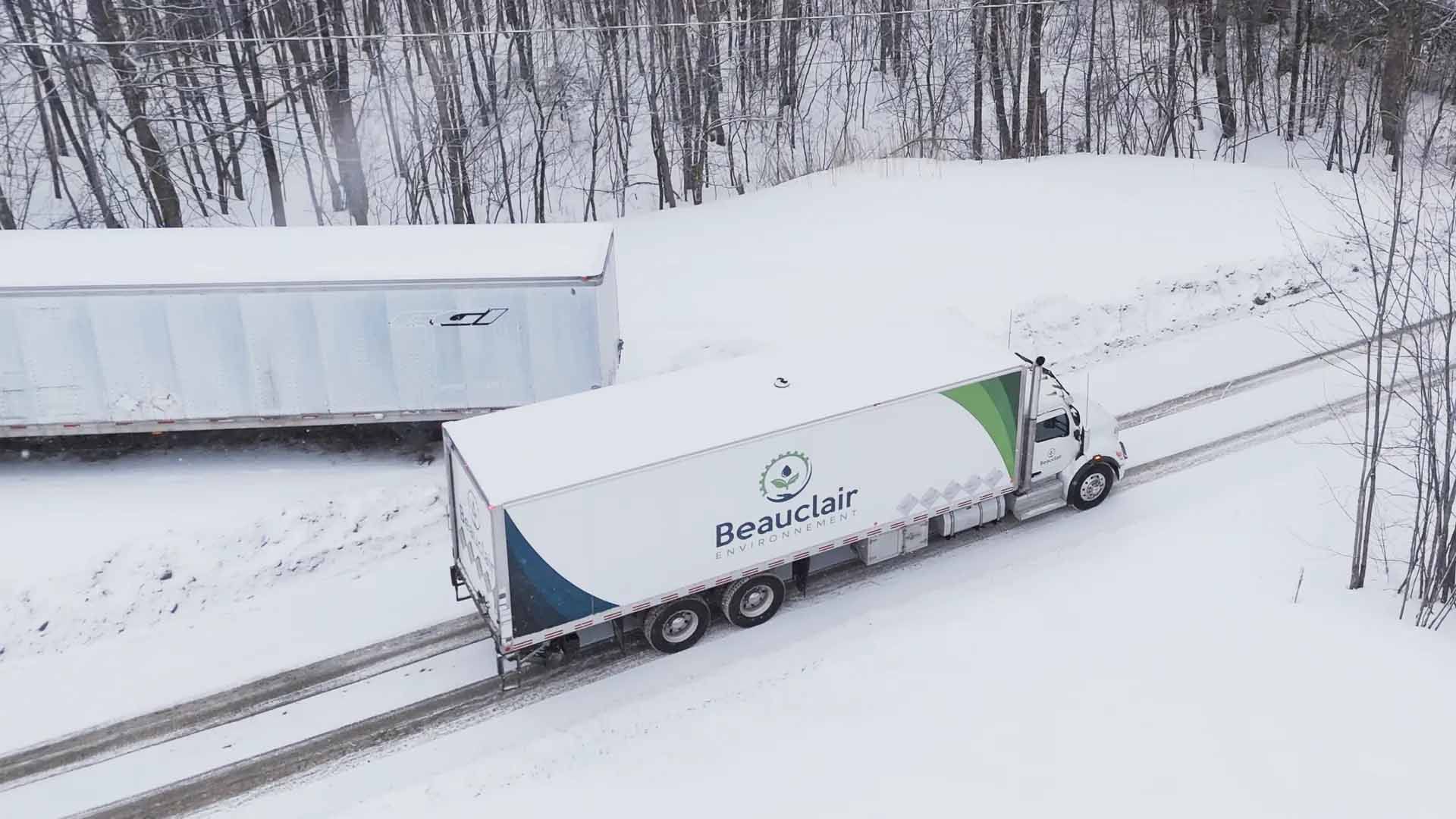 Camion portant le logo « Beauzeen » sur une route enneigée, remorque en arrière-plan.