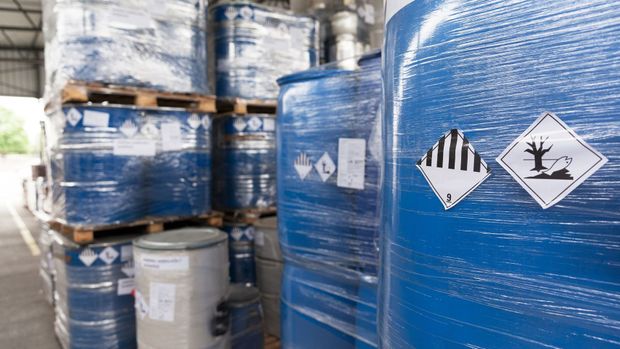 Un entrepôt rempli de nombreux barils bleus et de palettes de produits chimiques.