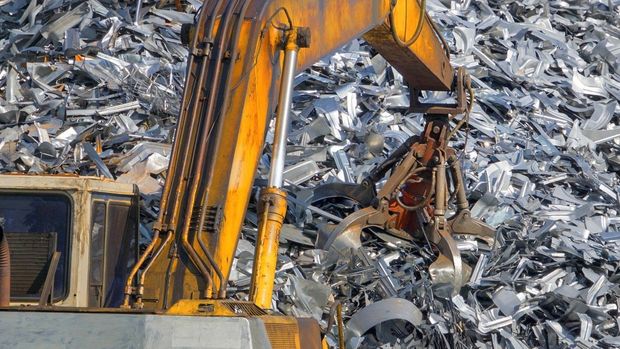 Une excavatrice jaune travaille sur un tas de ferraille.