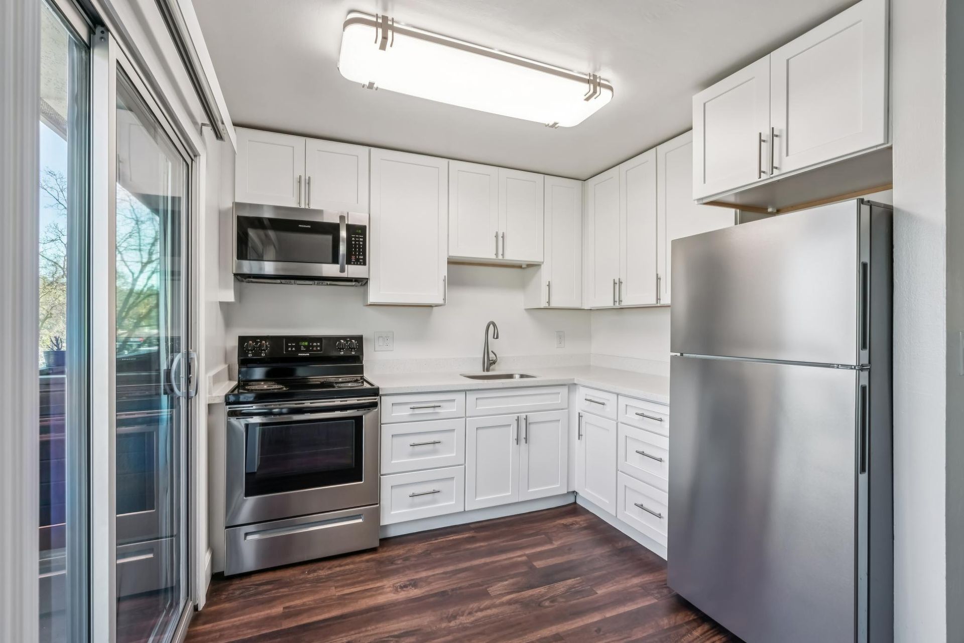 White kitchen with stainless steel appliances, dark wood floor, and access to a balcony.
