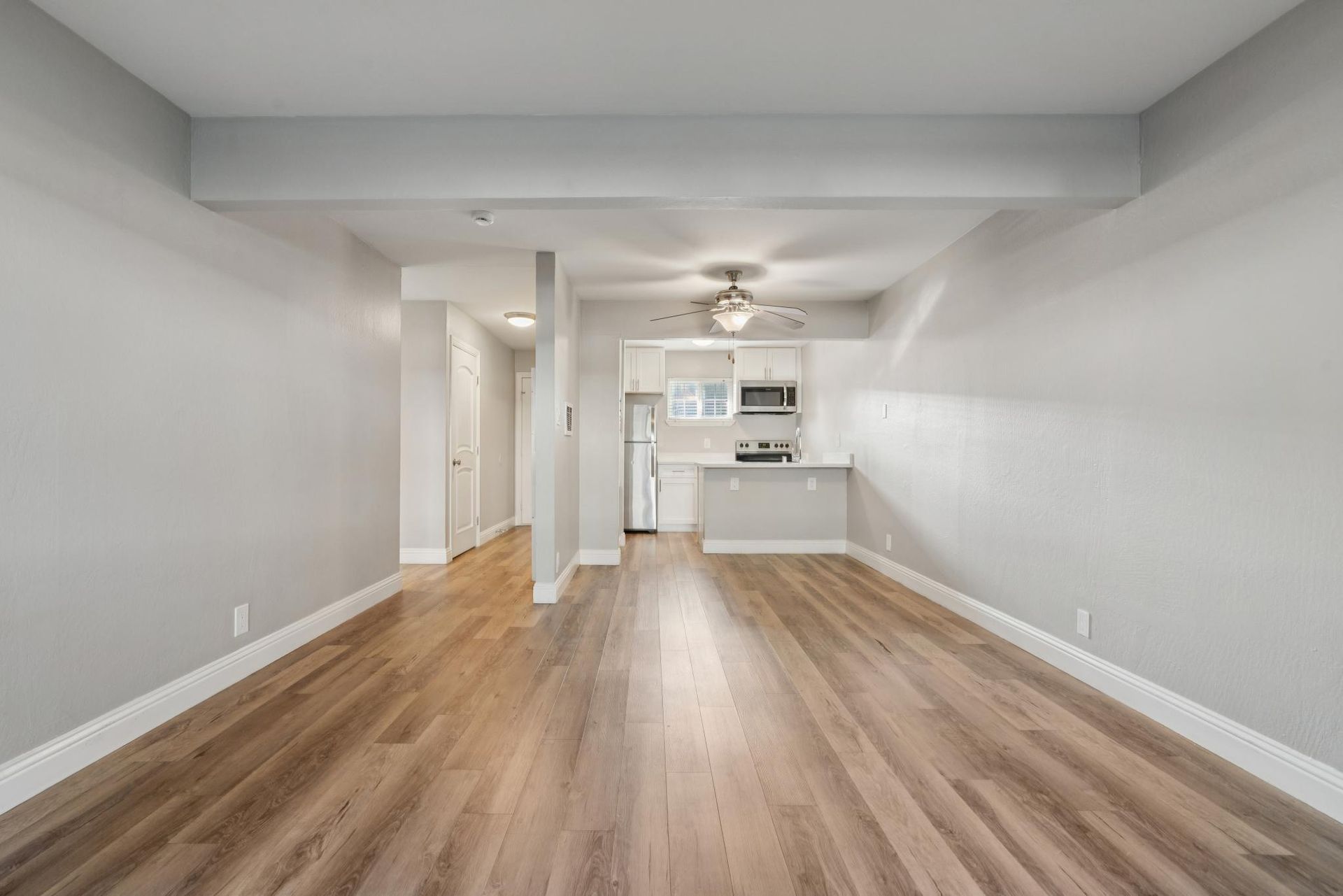 Empty apartment interior with wood flooring, light gray walls, and open kitchen.