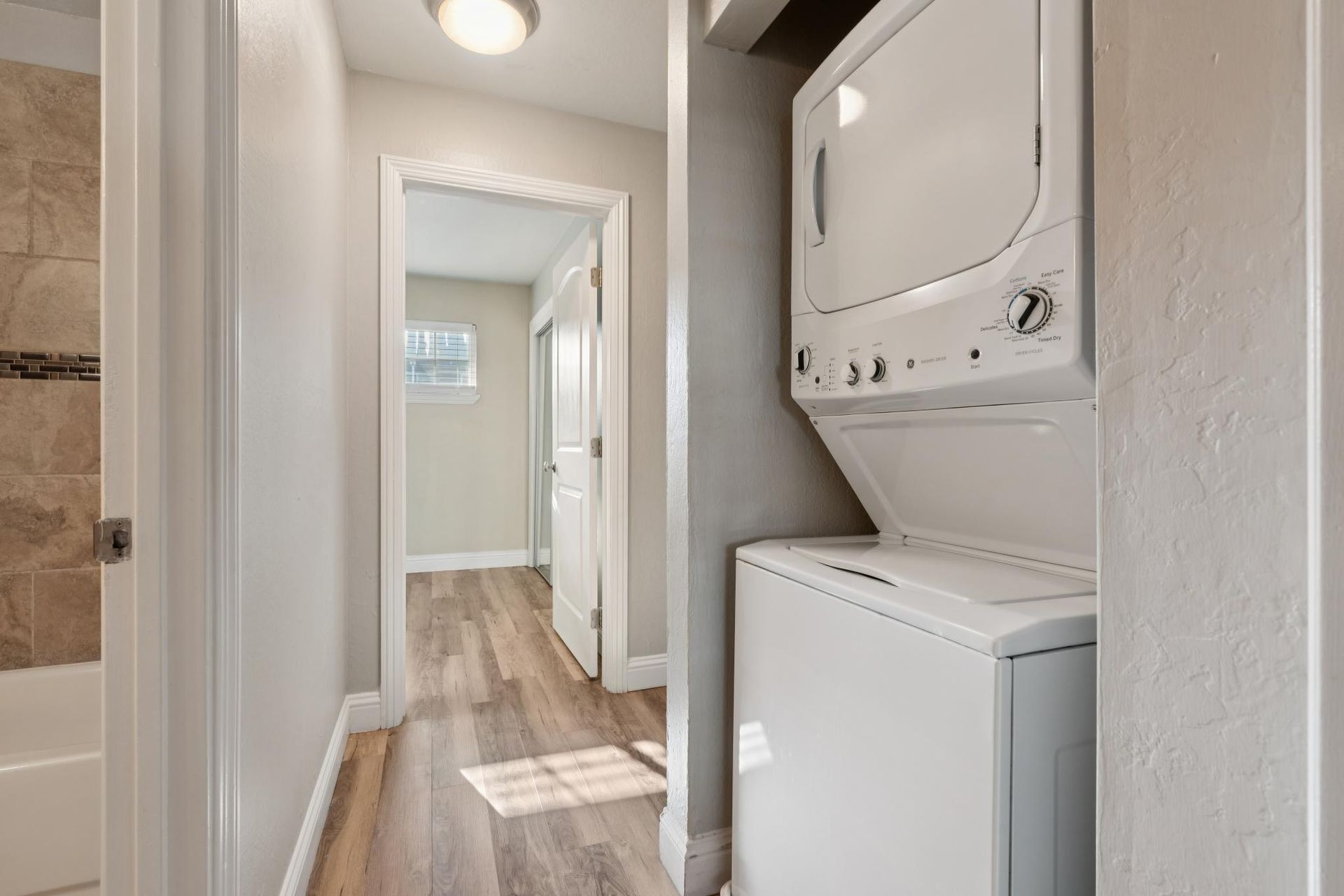 Hallway with stacked washer and dryer; bathroom on the left, door to another room straight ahead.