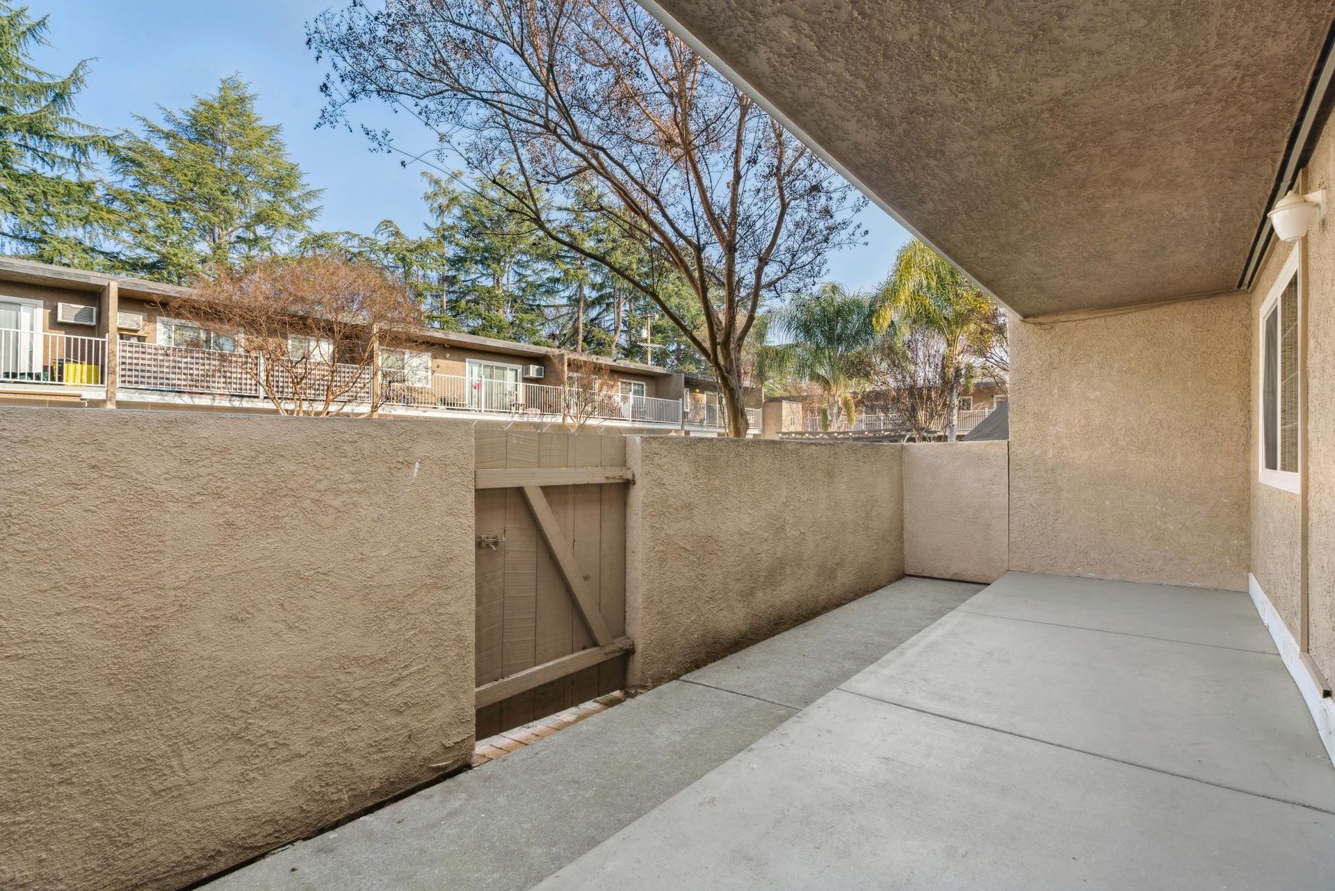 Covered patio with textured tan walls, concrete floor, small wooden door, and view of trees.