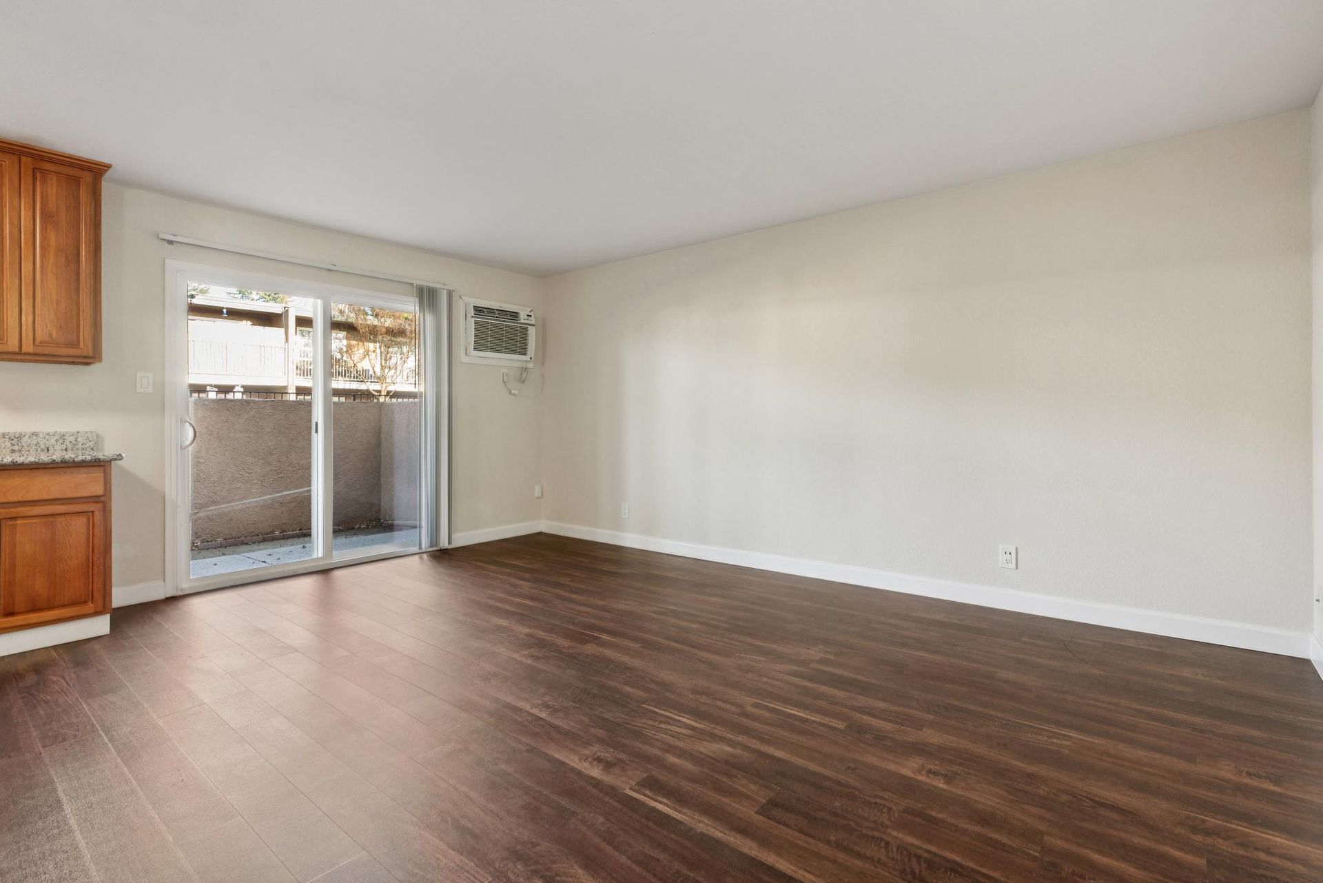 Empty living room with dark wood floor, light walls, and a sliding glass door to a balcony.