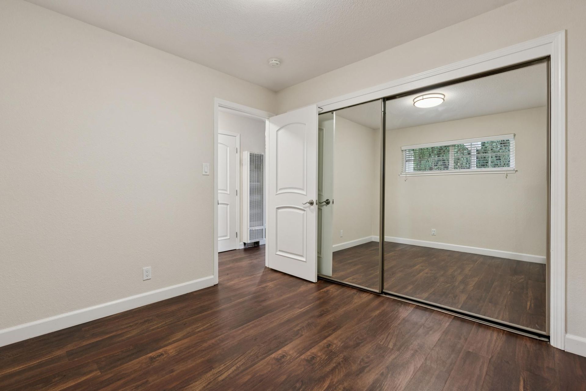 Bedroom with dark wood floors, mirrored closet doors, and a doorway to another room.