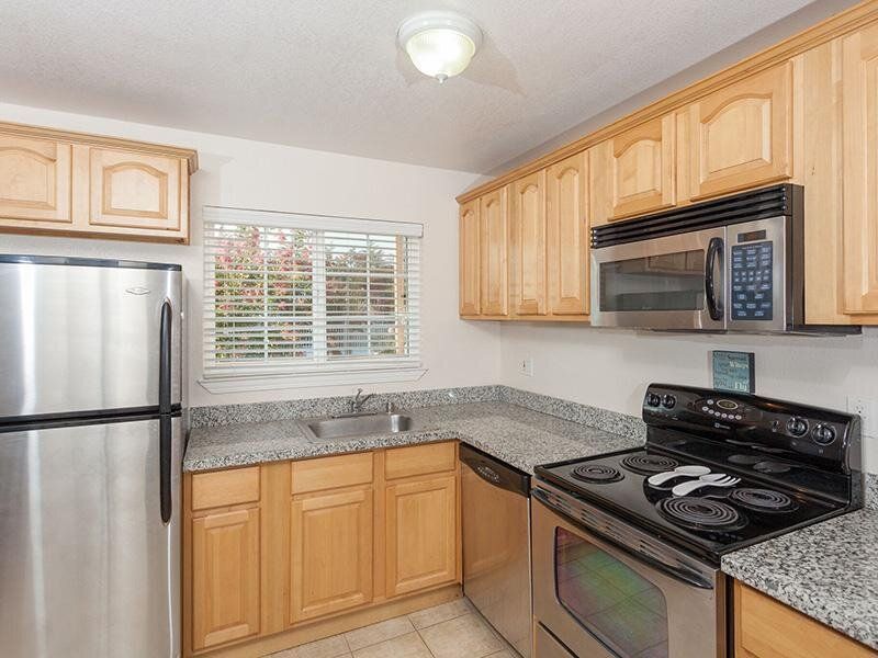 Kitchen with stainless steel appliances, granite countertops, wooden cabinets, and a window.