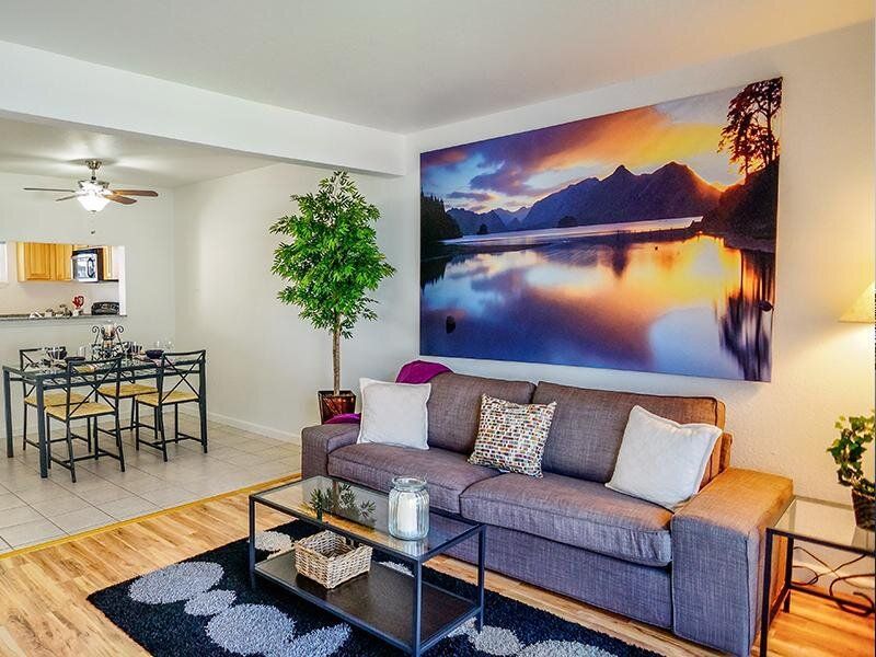 Open living room in an apartment with gray sofa, glass coffee table, and a large landscape wall art.
