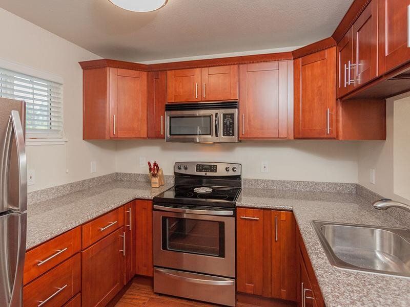 U-shaped kitchen with cherry wood cabinets, stainless steel refrigerator, stove, microwave, sink, and speckled countertops.