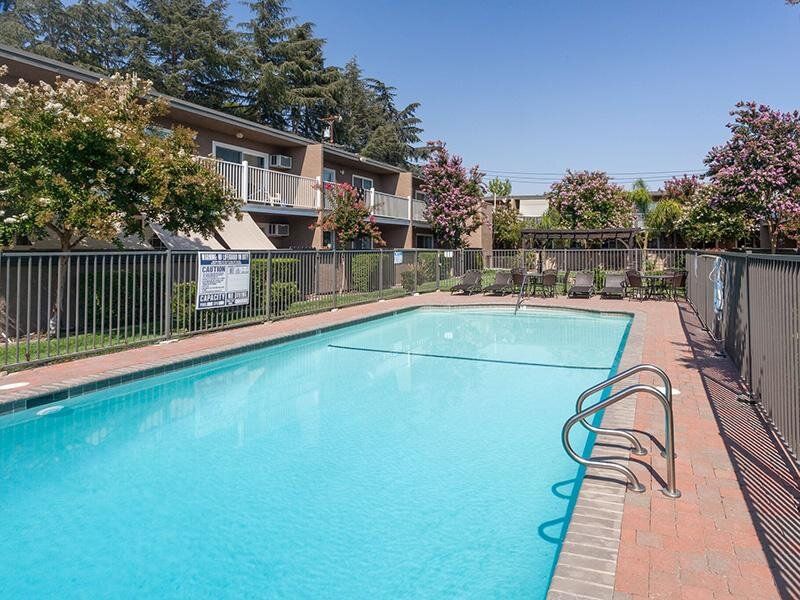 Outdoor rectangular pool at a residential complex, fenced with lounge chairs along the deck.