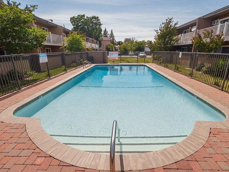 Outdoor community pool with metal fence and brick-paver deck.
