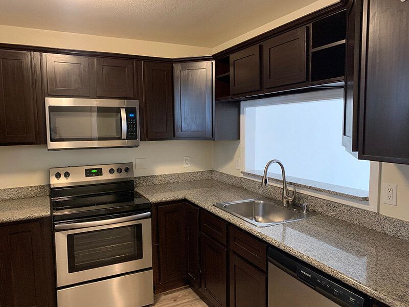 Modern apartment kitchen with dark wood cabinets, stainless steel appliances, and a double sink.